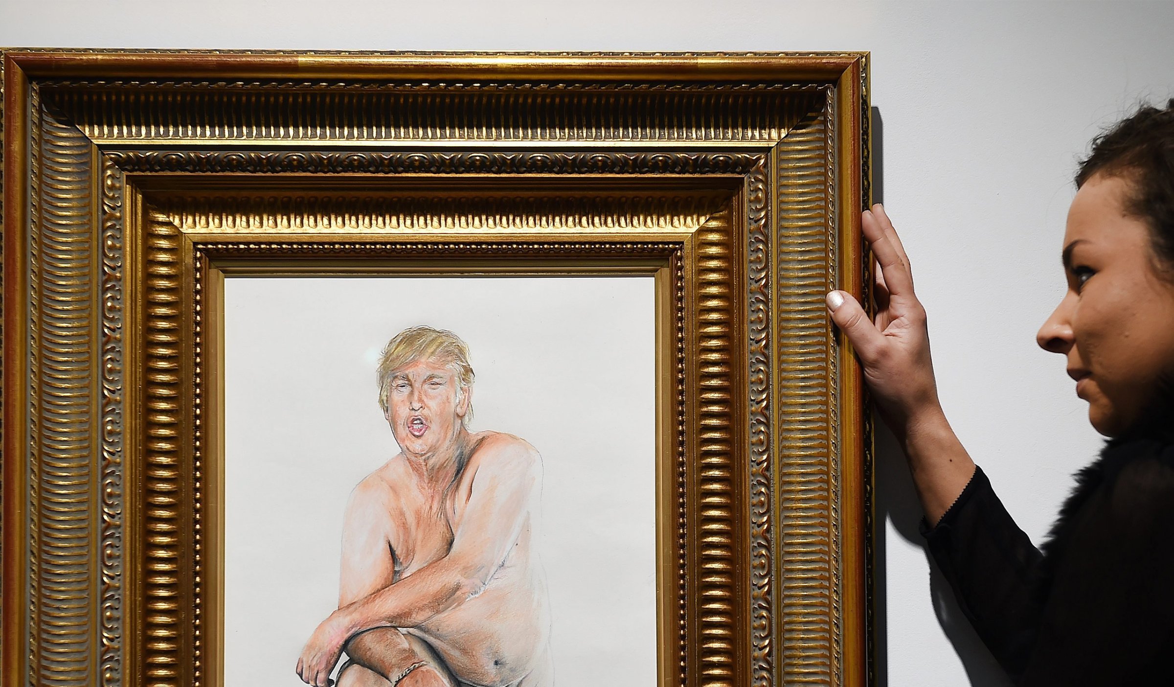 A woman adjusts a painting depicting a naked man with the head of Donald Trump by US artist Illma Gore at the Maddox Gallery in London, April 11, 2016.