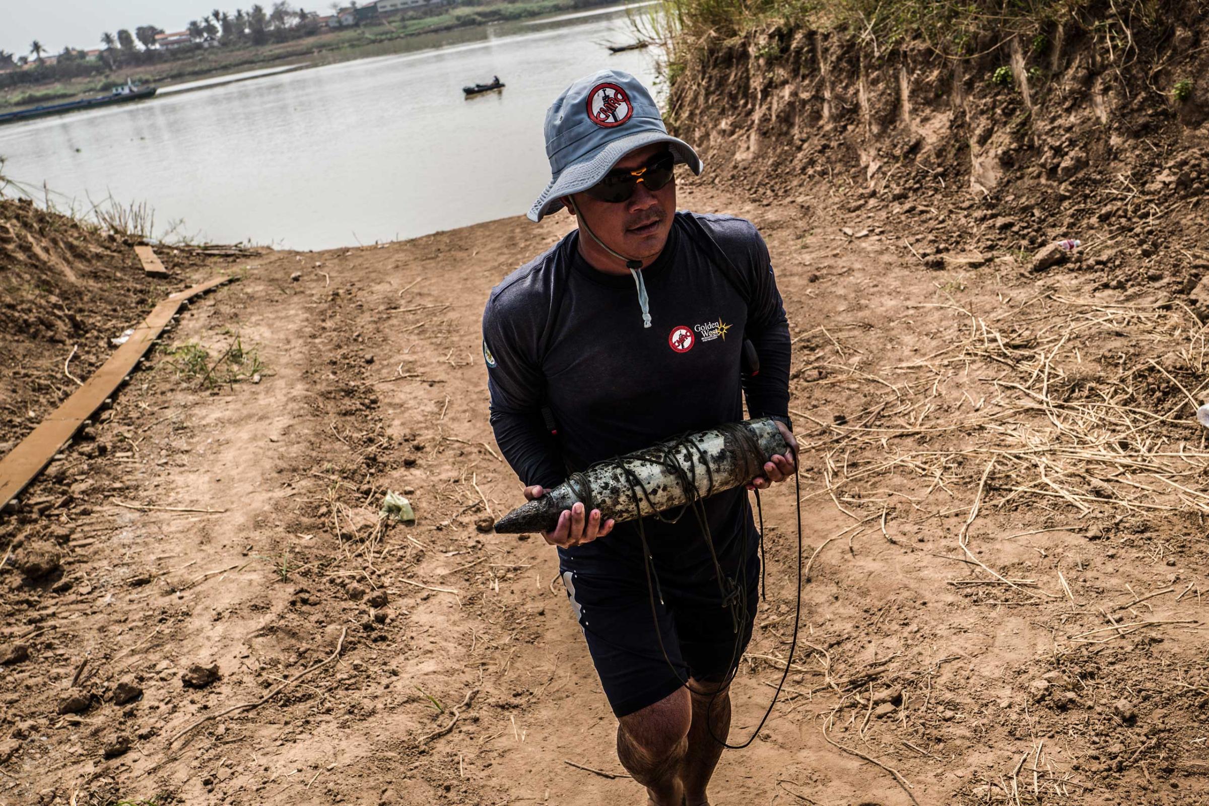 Team Leader Sok Chenda carries a 105mm round from the banks of the Tonle Sap River in March 2016. The team was informed of the round whilst conducting reconnaissance in the area.
