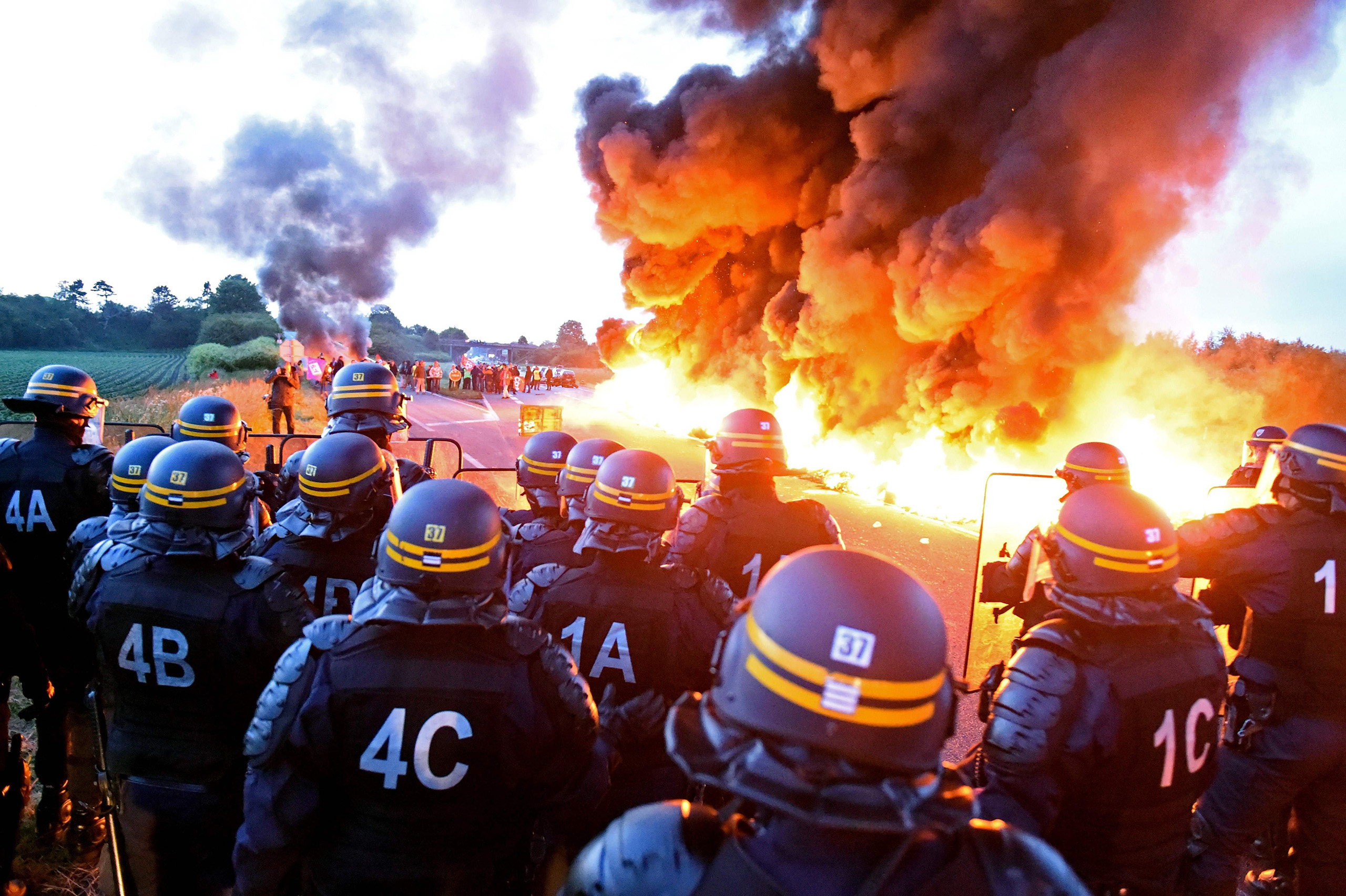 Riot police stand guard behind a fire as refinery workers hold a blockade of the oil depot of Douchy-Les-Mines, in northern France, to protest against the government's proposed labor reforms on May 25, 2016. (François Lo Presti—AFP/Getty Images)