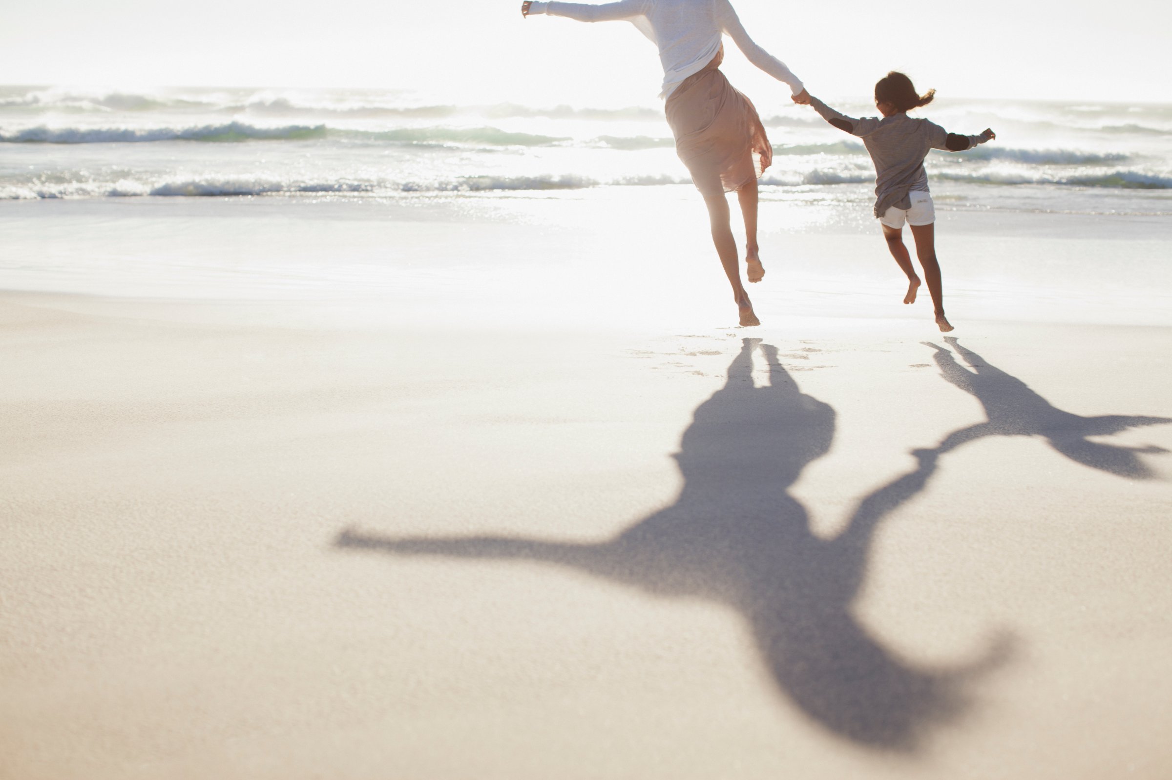 Mother and daughter holding hands and running on sunny beach