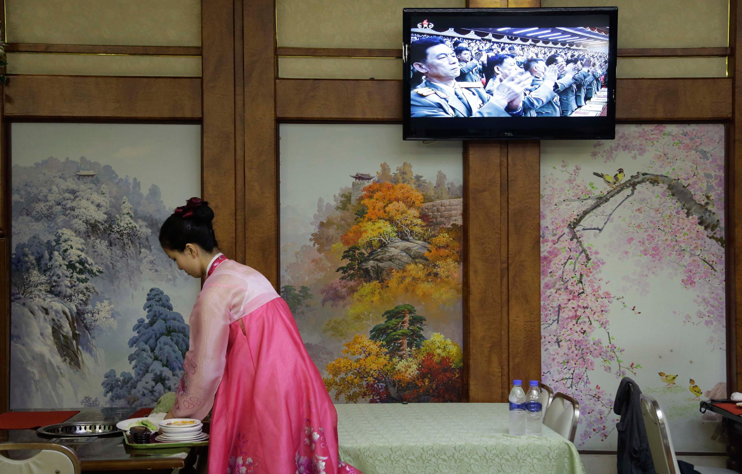 A waitress clears a table while a broadcast of the second day of the 7th Congress of the Workers' Party of Korea is shown on local television on Saturday, May 7, 2016, in Pyongyang, North Korea. North Korea's ruling party is preparing to bestow its top title on leader Kim Jong Un, another clear sign that the third heir to North Korea's dynasty of Kims is firmly in control despite his country's deepening international isolation over one of his key ambitions, to keep developing more and better nuclear weapons. (AP Photo/Wong Maye-E)