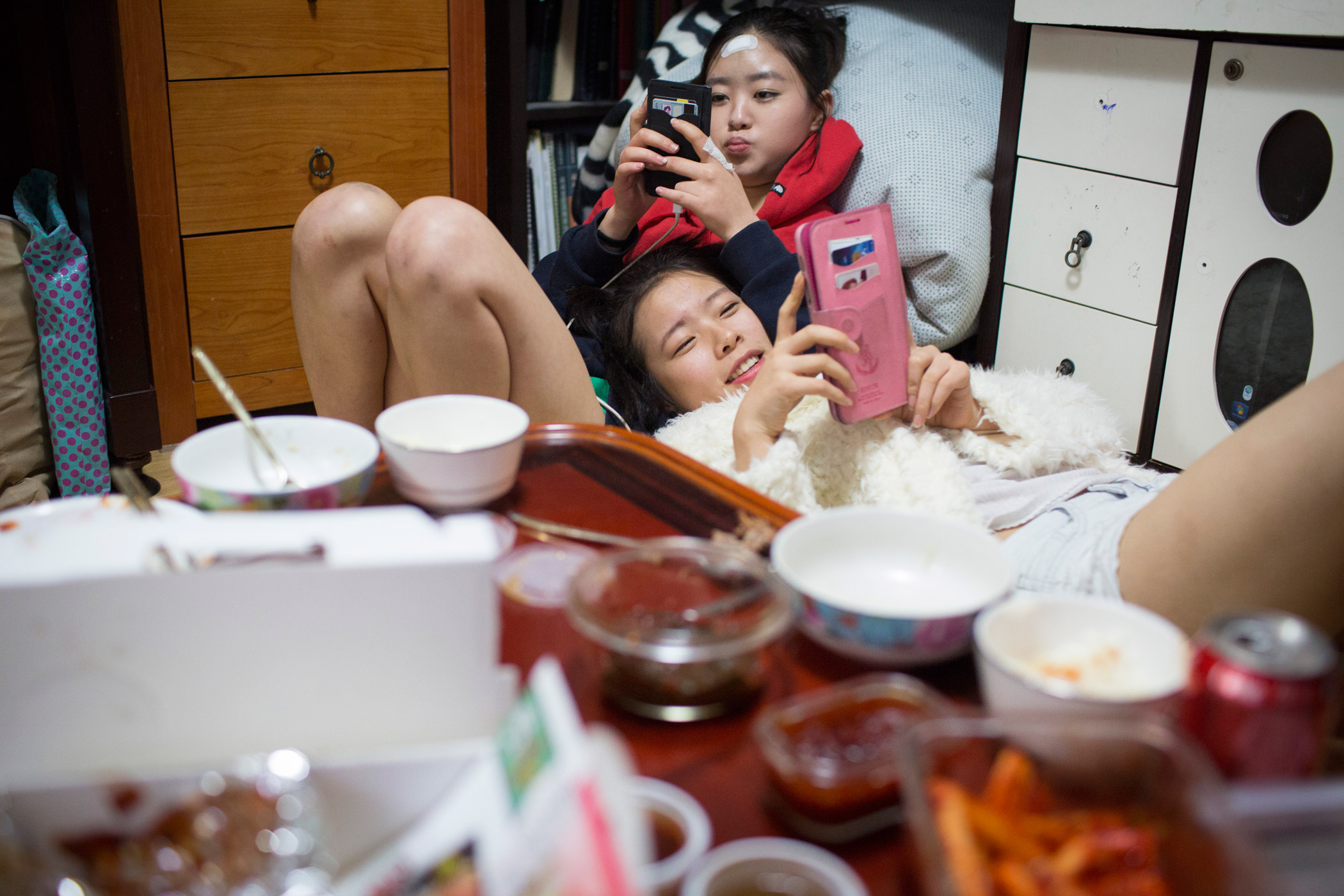 Kyong-ok and Sarah spend time on their phones after sharing takeout for dinner at Kyong-ok's apartment on Feb. 28, 2015 in Mia, Seoul, South Korea. Caitlin O'Hara