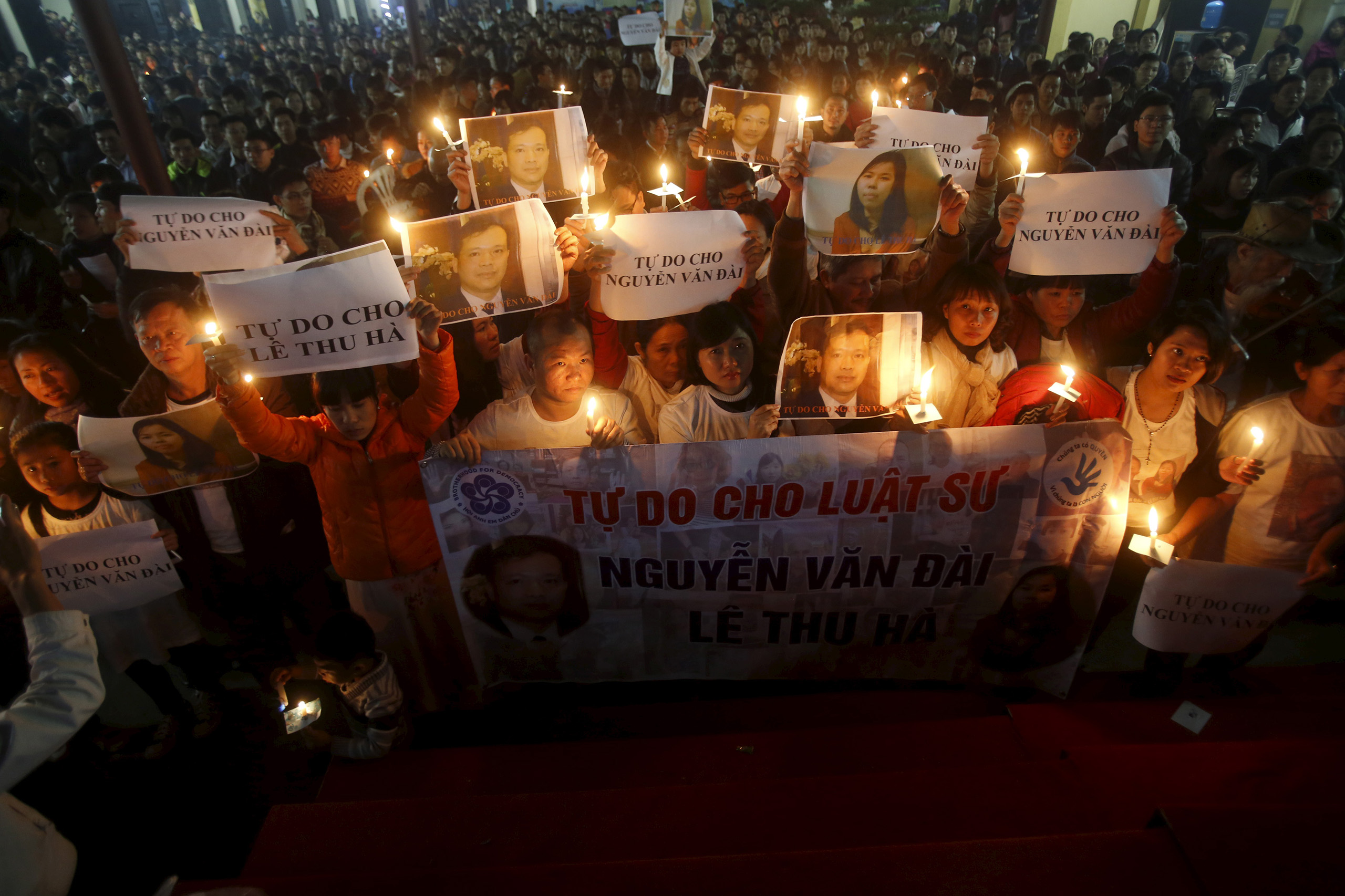 Khanh holds an image of her husband Dai as Catholics hold candles and image of Dai's assistant Ha during a mass prayer for Dai and Ha at Thai Ha church in Hanoi