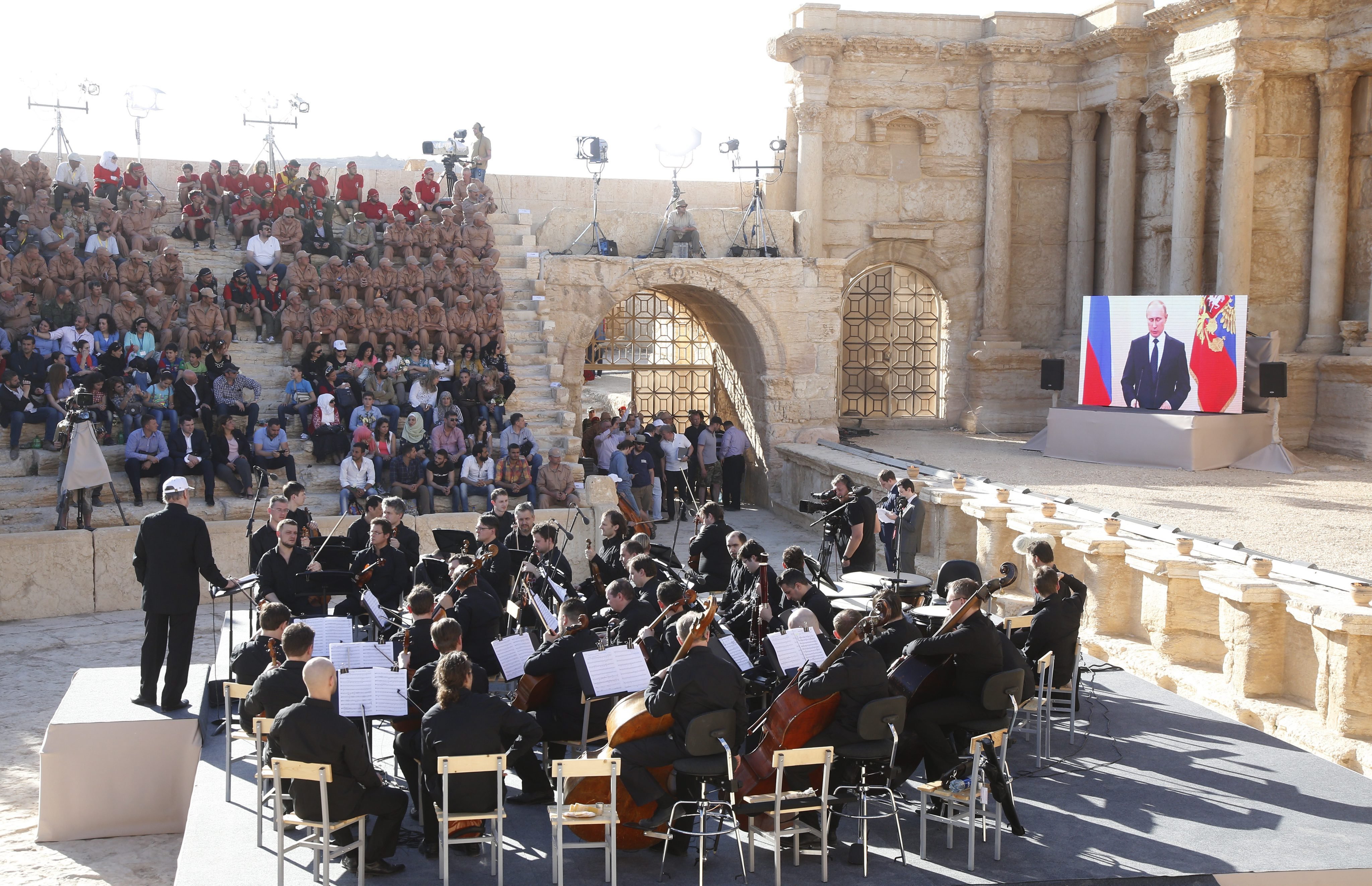 Russian President Vladimir Putin, via a live video feed (screen at right), delivers a speech during a concert by the Mariinsky Theater Orchestra in Palmyra amphitheater in Syria, on May 5, 2016. (Sergei Chirikov—EPA)