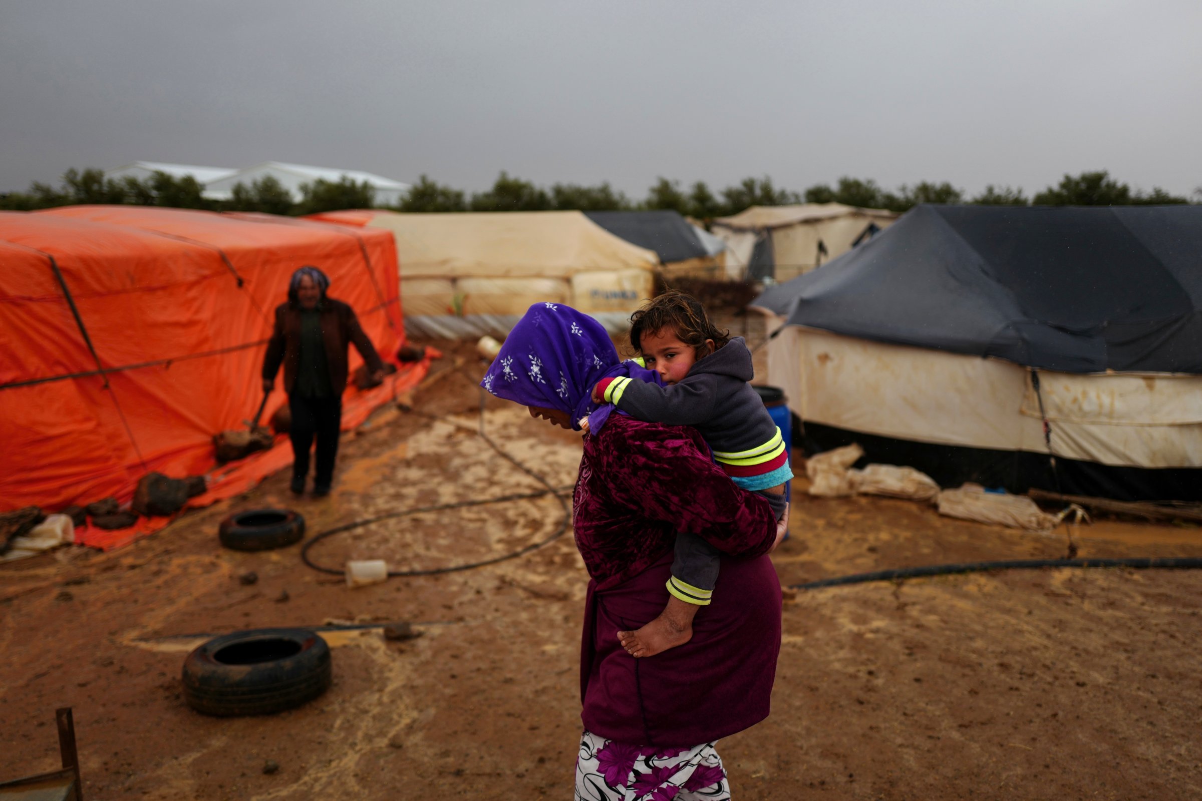 A Syrian refugee carries her child as she heads back to her tent through muddy grounds during a rainfall at an informal tented settlement near the Syrian border, on the outskirts of Mafraq, Jordan, March 28, 2016.