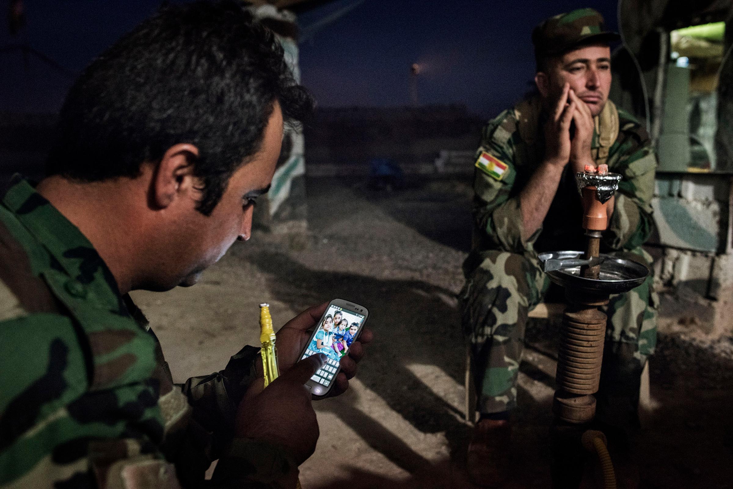 Sgt. Farsal Goran looks at his cellphone as he sits with Majid Hamid, 32, while shisha is smoked at the front outside Makhmour, Iraq, May 8, 2016.