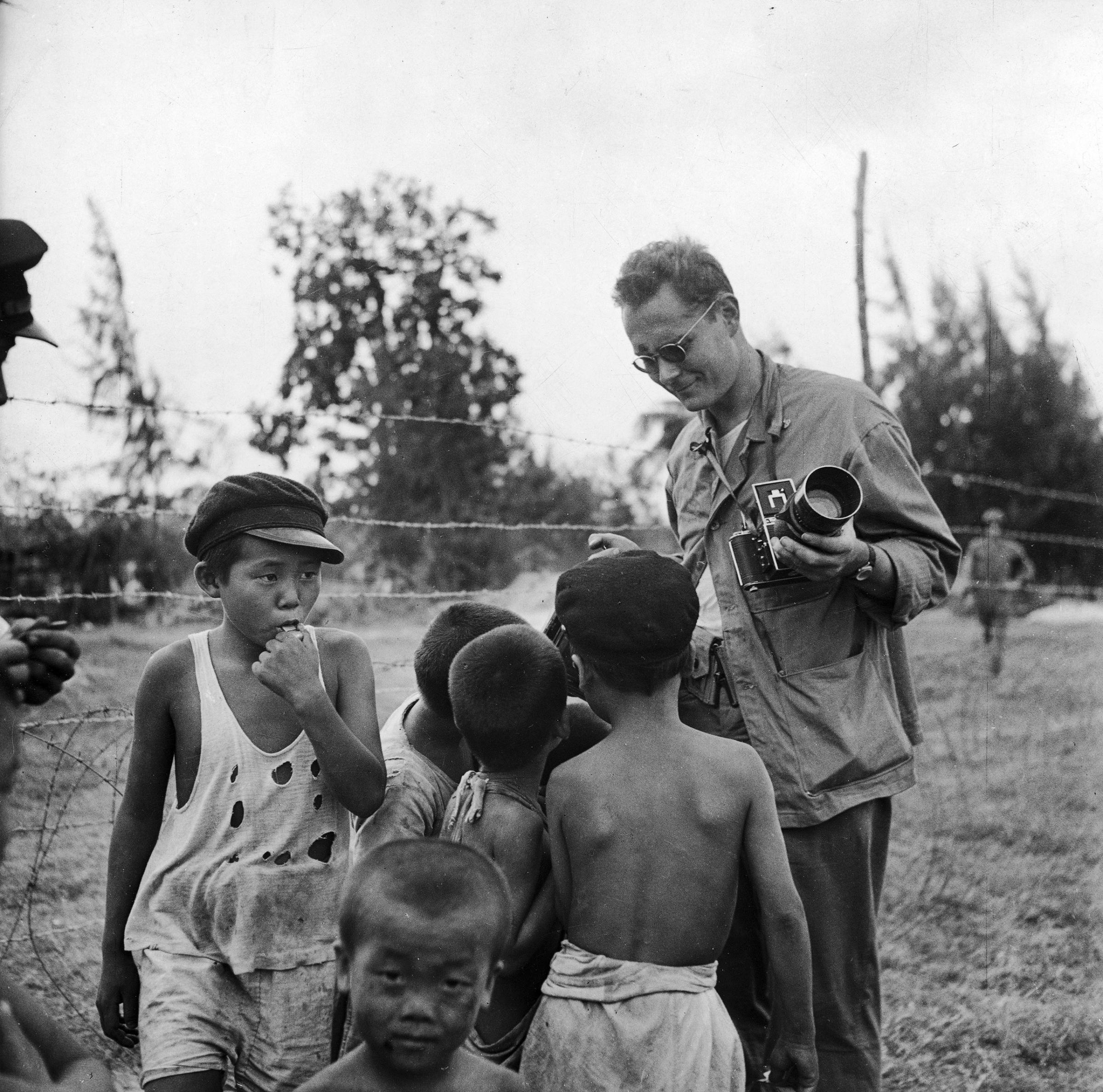 LIFE photographer W. Eugene Smith talking with and giving treats to local children after battle between Japanese and American forces for control of Saipan.