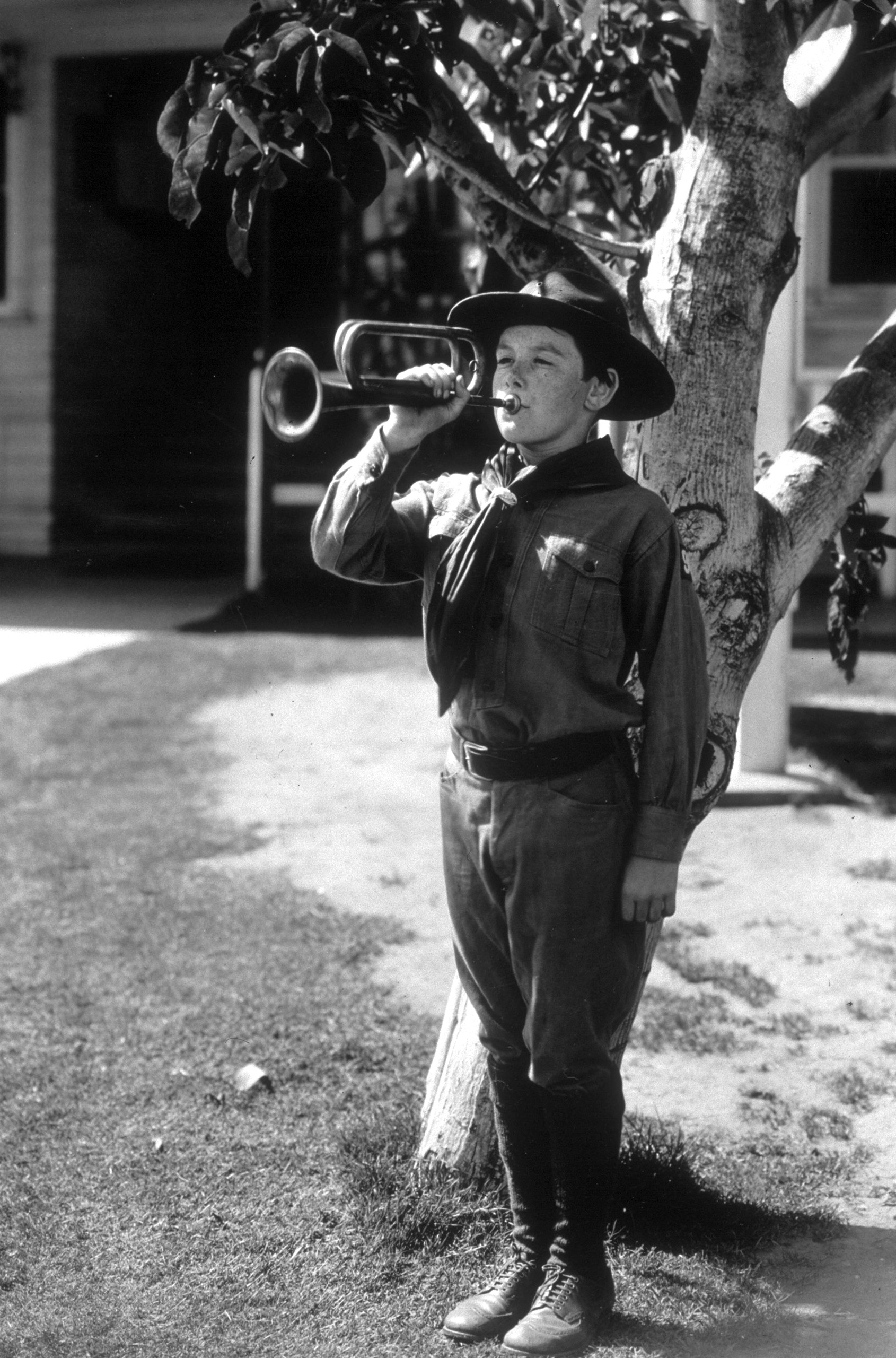 Child actor Junior Coghlan playing the trumpet in a scout uniform. Circa 1935.