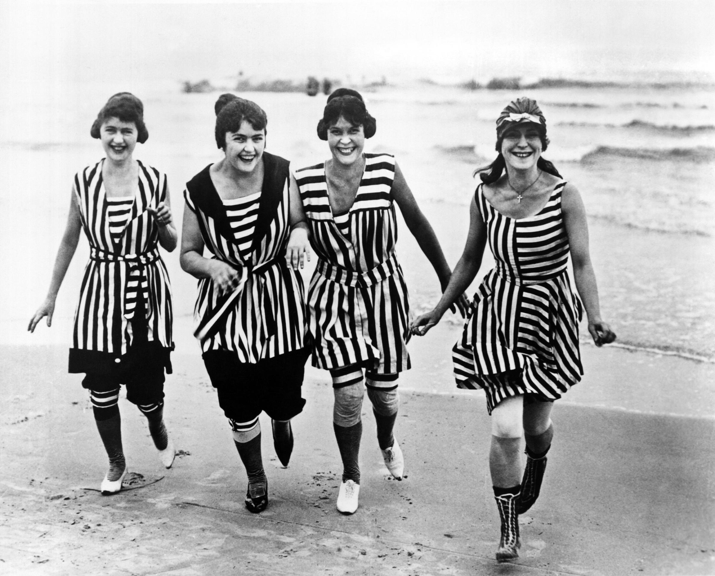 Four young women in matching beach wear run out of the surf, Los Angeles, California, circa 1910.