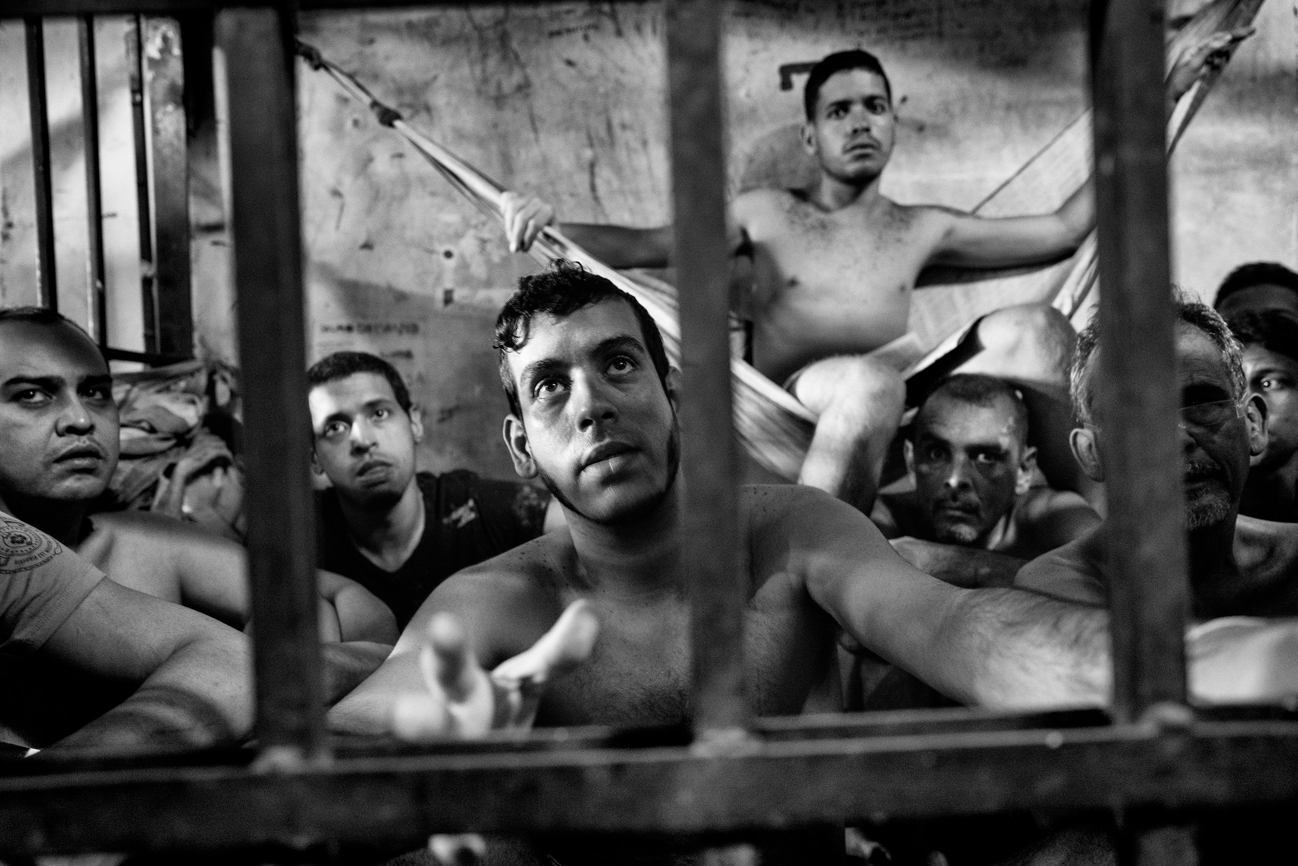 Prisoners inside a crowded cell at the Chacao municipal police station in eastern Caracas. There is no room to  sit and prisoners take turns resting on sheets tied to bars like hammocks.  Jails in Venezuela are seriously overcrowded with shortages of food and medicine. Because of the economic and political crisis, the number of prisoners grows daily as more Venezuelans are arrested for crimes, including mugging, kidnapping and murder, June 2016. From  Witnessing a ‘Complete Collapse of Society’ in Venezuela