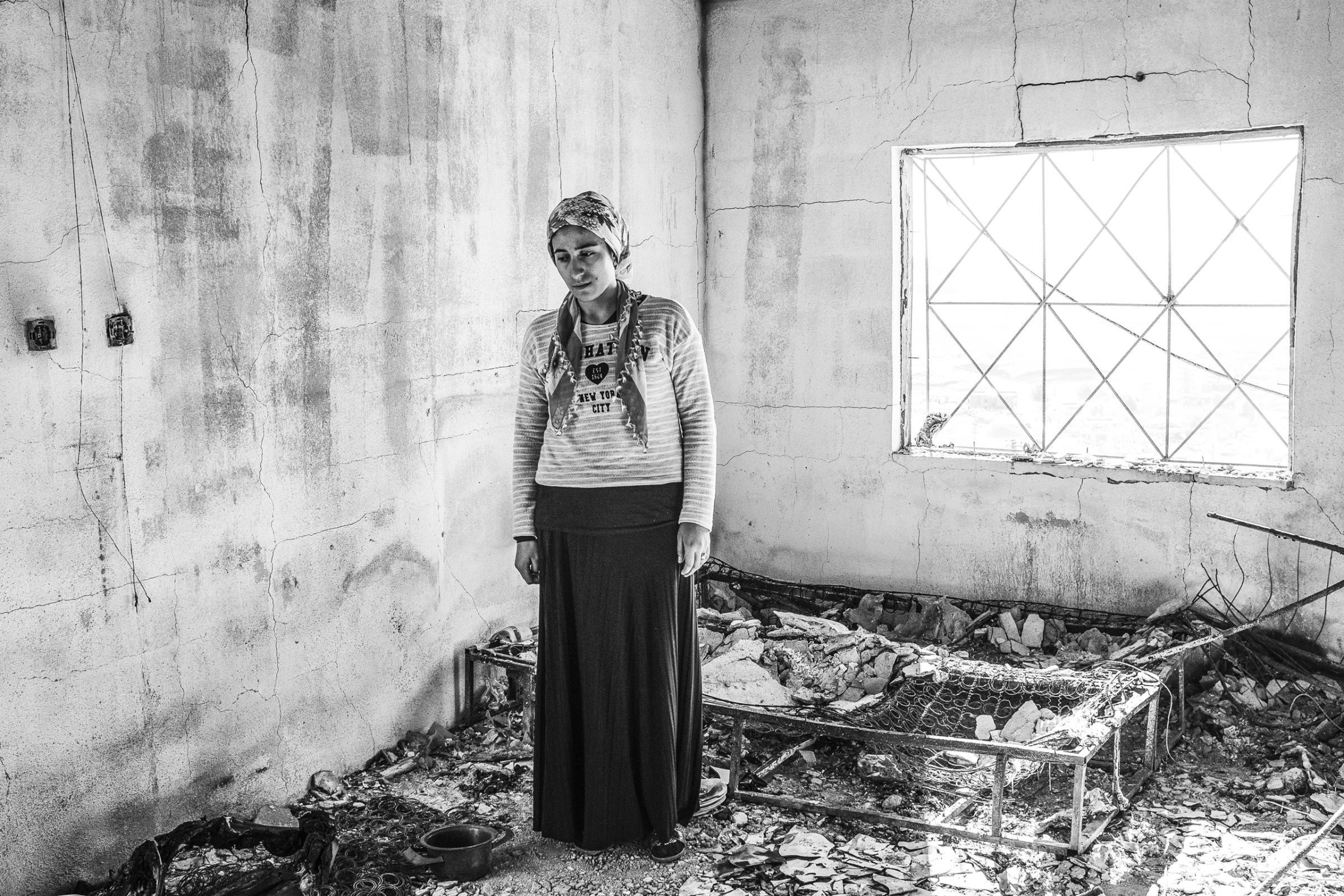 Zahide Onen stands in the wreckage of her home that was hit by a Turkish military rocket, while she and her family slept, Derik, Turkey, Dec. 2015.