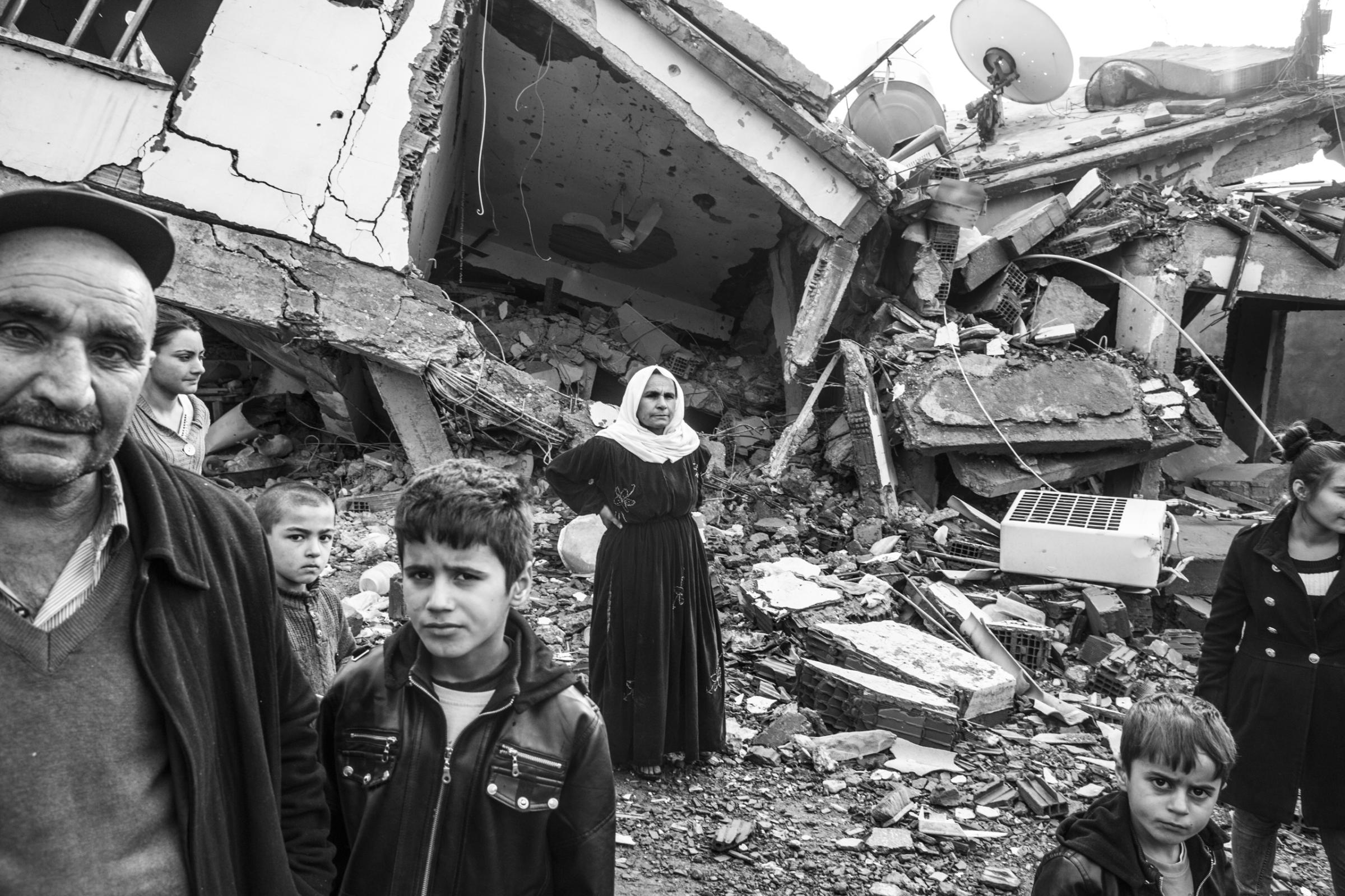 A family stands near their home that was damaged during fighting between government troops and separatist Kurdistan Workers Party (PKK) fighters, in the Kurdish town of Silopi, near the border with Iraq, Jan. 2016