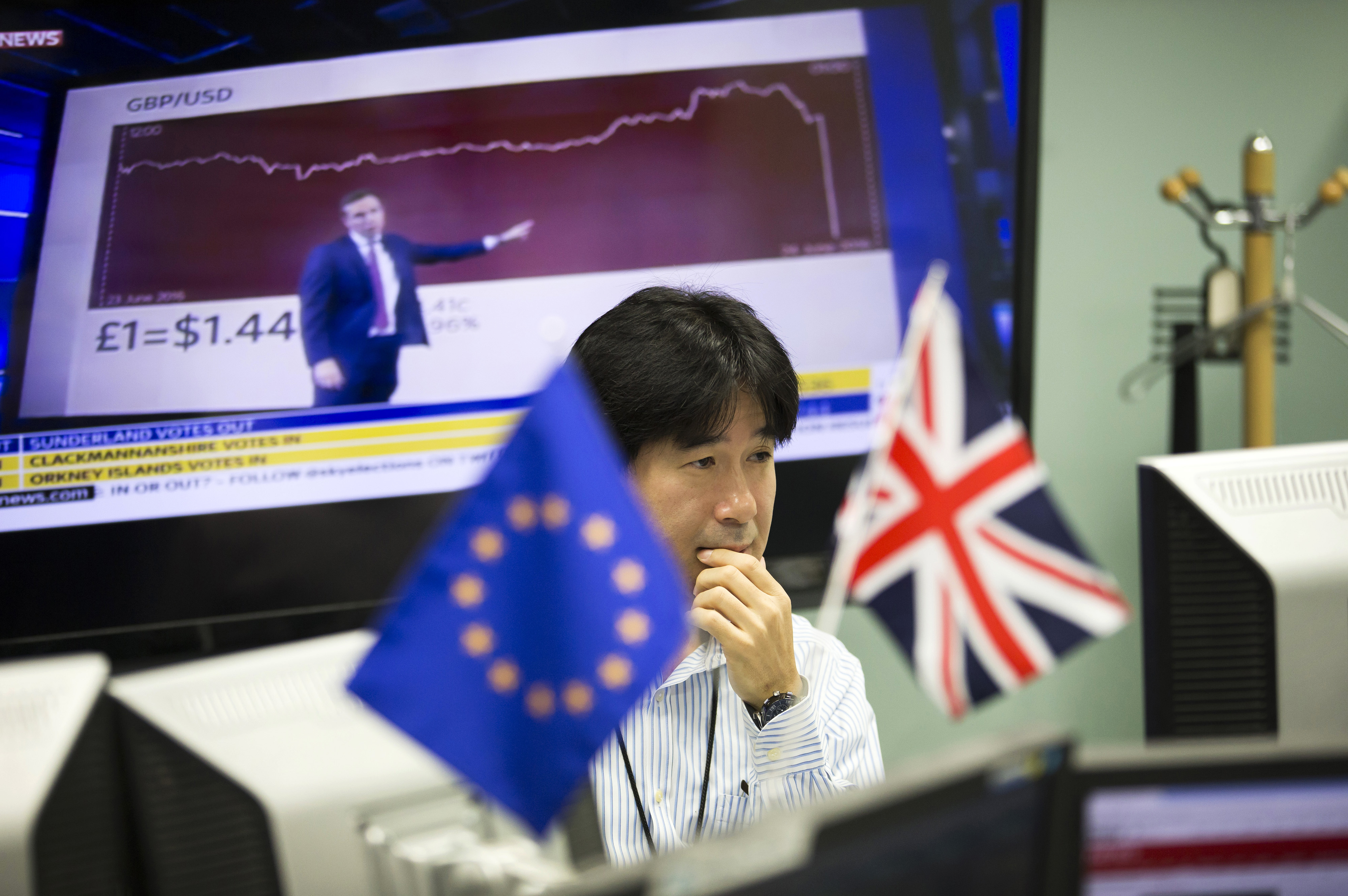 An employee works in front of computer monitors near a European Union flag, left, and a British Union flag at a foreign-exchange brokerage in Tokyo on June 24, 2016 (Bloomberg/Getty Images)