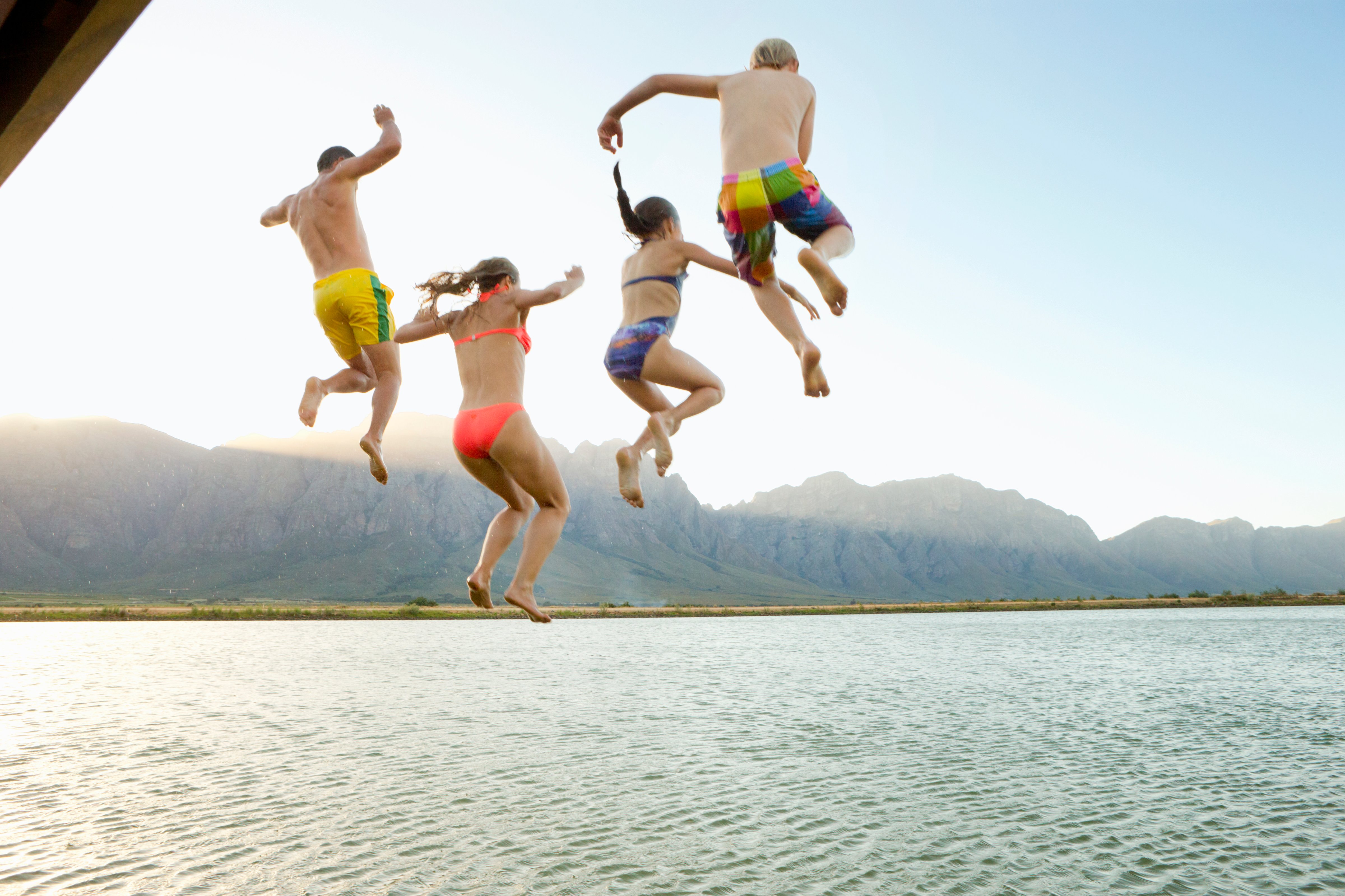 Family, in swimwear, jumping into a lake from a jetty