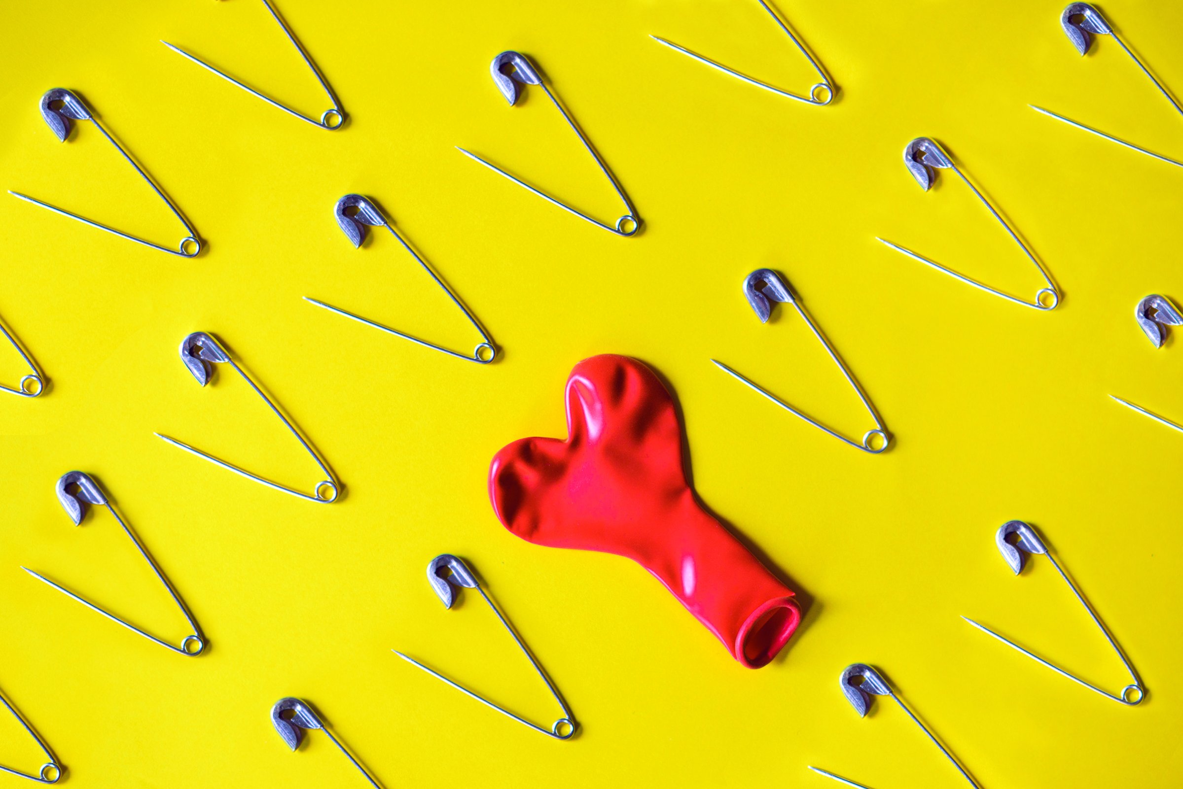 Open safety pin and red deflated balloon on yellow background