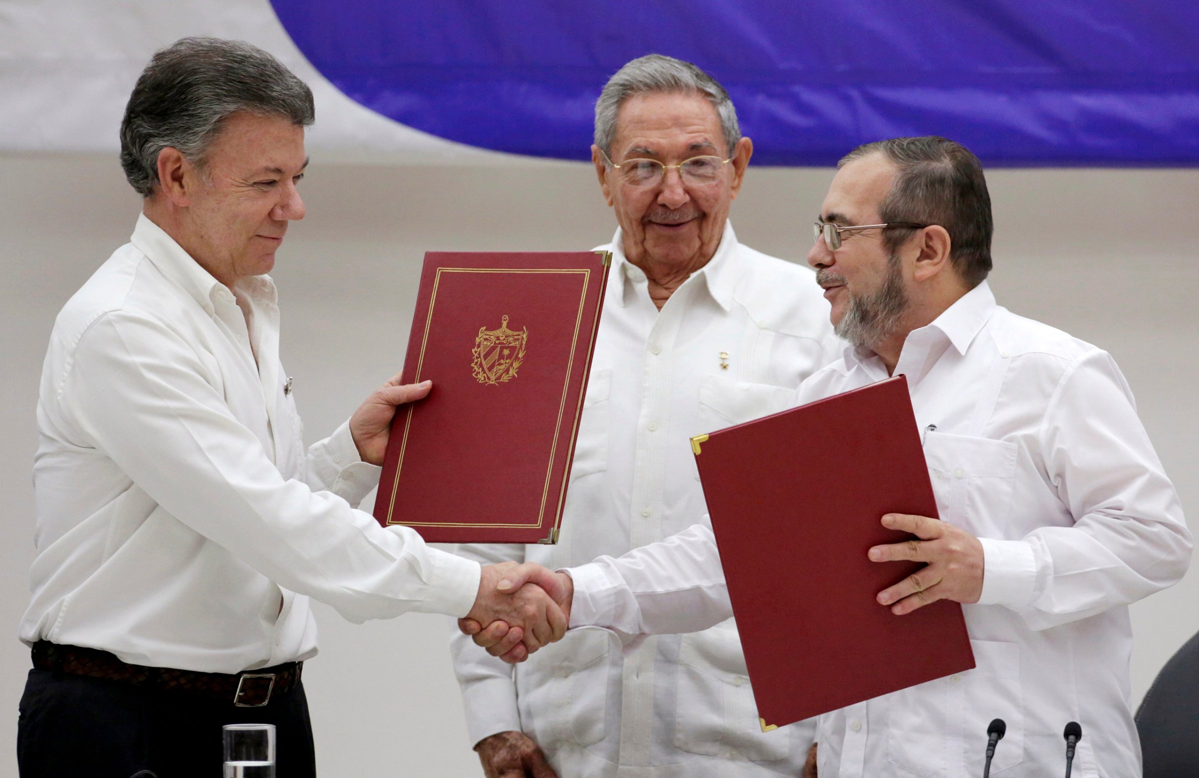Colombia's President Juan Manuel Santos, left, shakes hands with FARC rebel leader Rodrigo Londono, better known by his nom de guerre Timochenko, right, as Cuba's President Raul Castro looks on after the signing of a historic ceasefire deal between the Colombian government and FARC rebels in Havana, Cuba, on June 23, 2016.