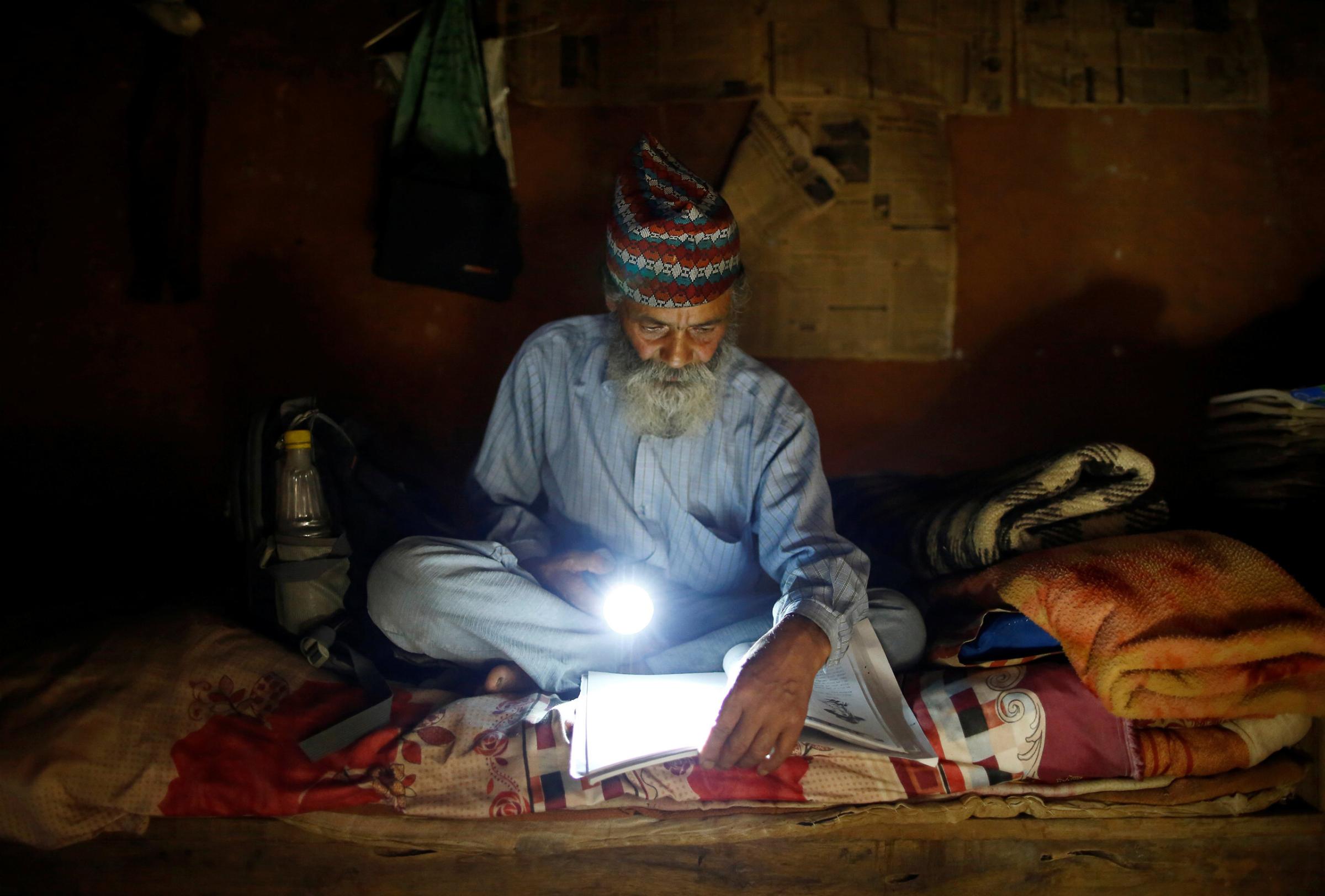 Durga Kami, 68, who is studying in the tenth grade at Shree Kala Bhairab Higher Secondary School, uses a torch to read a book during a power cut, at his one-room house in Syangja, Nepal, June 4, 2016. REUTERS/Navesh Chitrakar. SEARCH "DURGA KAMI" FOR THIS STORY. SEARCH "THE WIDER IMAGE" FOR ALL STORIES