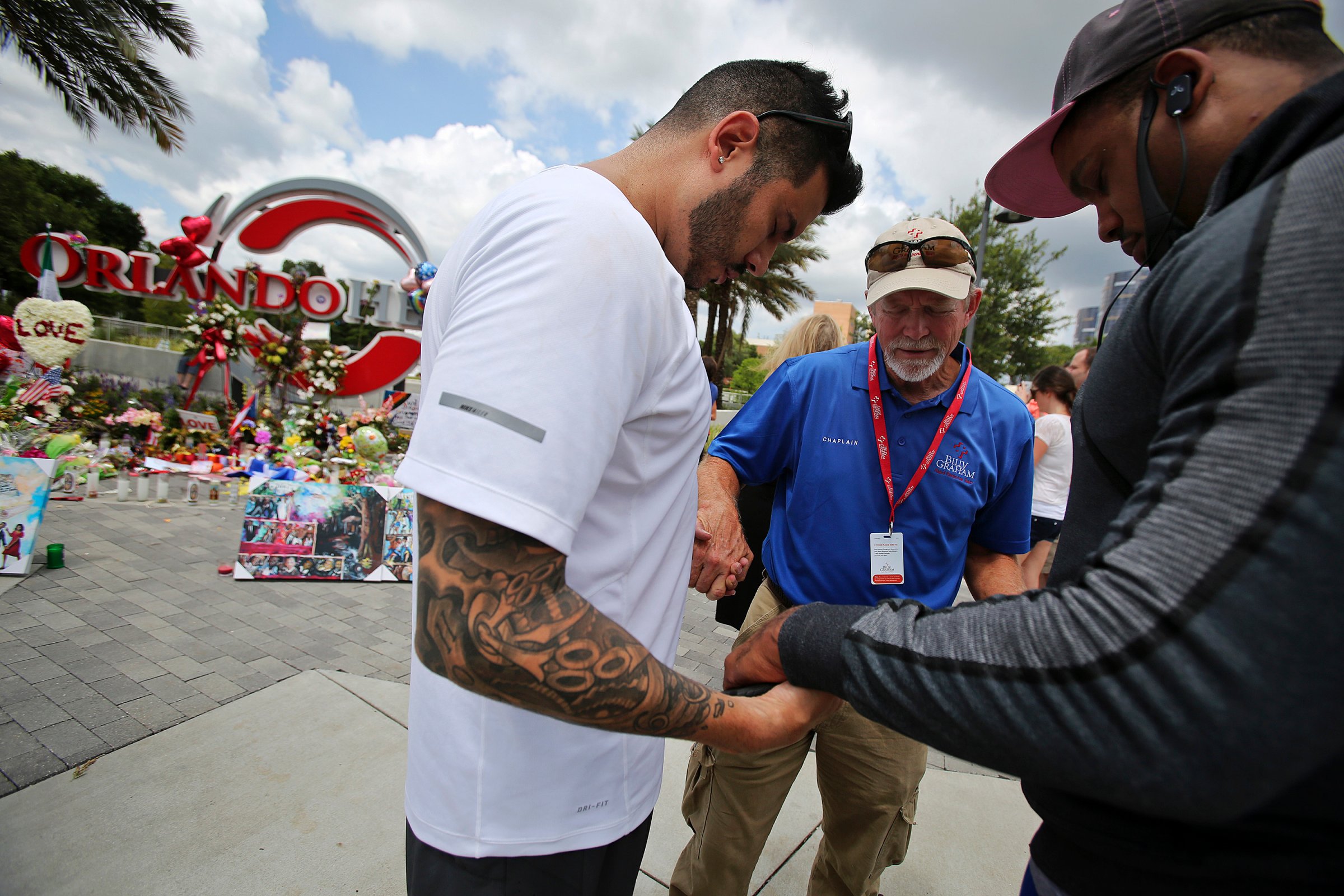 Carl Hill, center, with the Billy Graham Rapid Response Team, prays with Ricky Padilla, left, and Nathan Watson, right, by a memorial set up at the Orlando Health sign at the corner of Orange Avenue and Miller Street in Orlando on June 16, 2016.