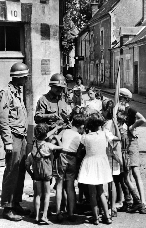French children scramble around a sergeant, right, a US Army military policeman, as he breaks open a 'K' ration package for distribution in a street of Orleans