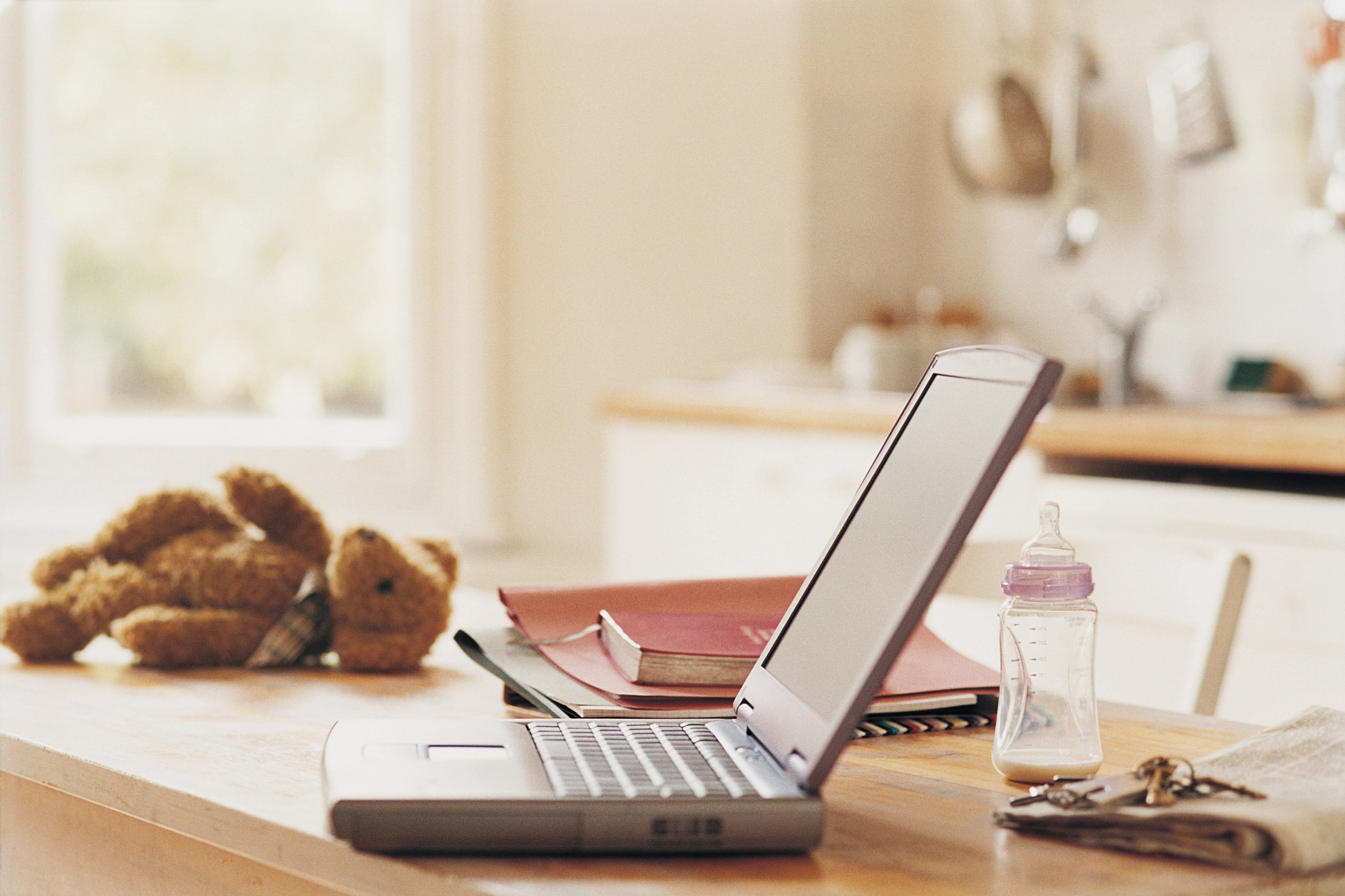 Laptop, Teddy Bear, Baby Bottle, Newspaper, Keys, a Book and a Folder on a Kitchen Counter