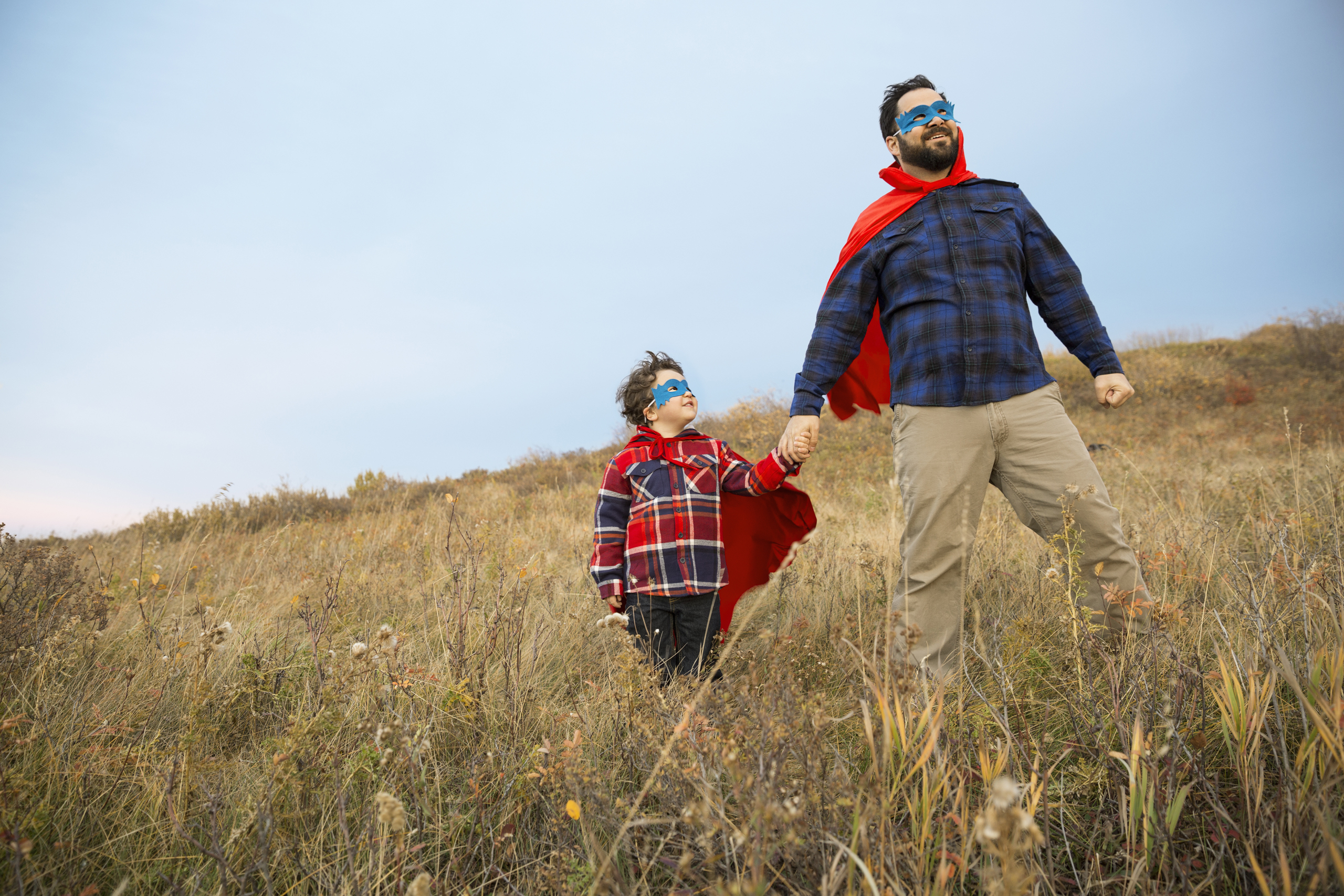 Father and son in superhero capes in field