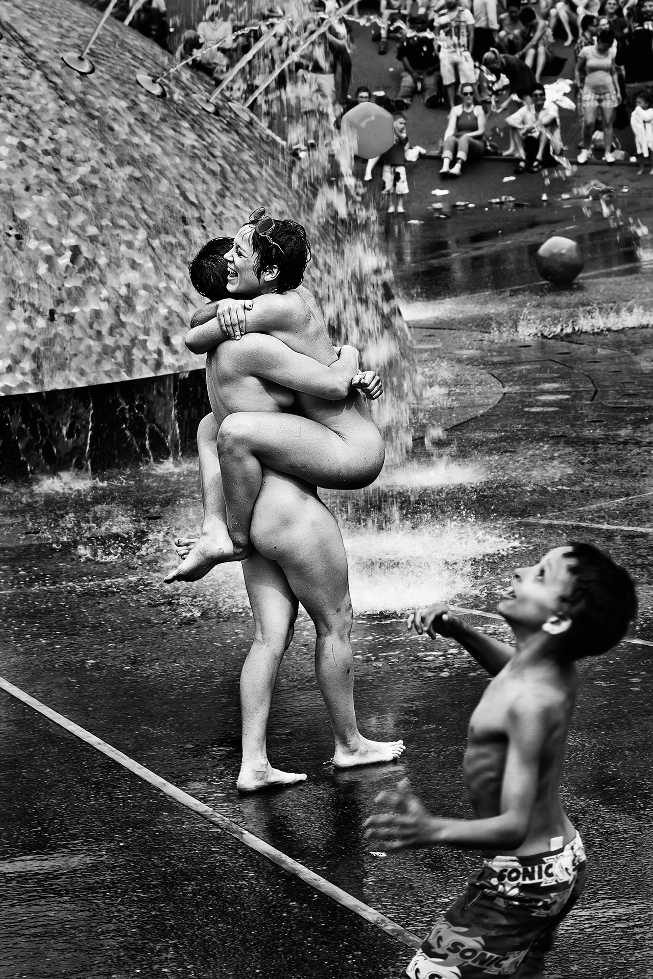 Two women embrace while a boy plays ball at the International Fountain at Seattle PrideFest on June 26, 2011.