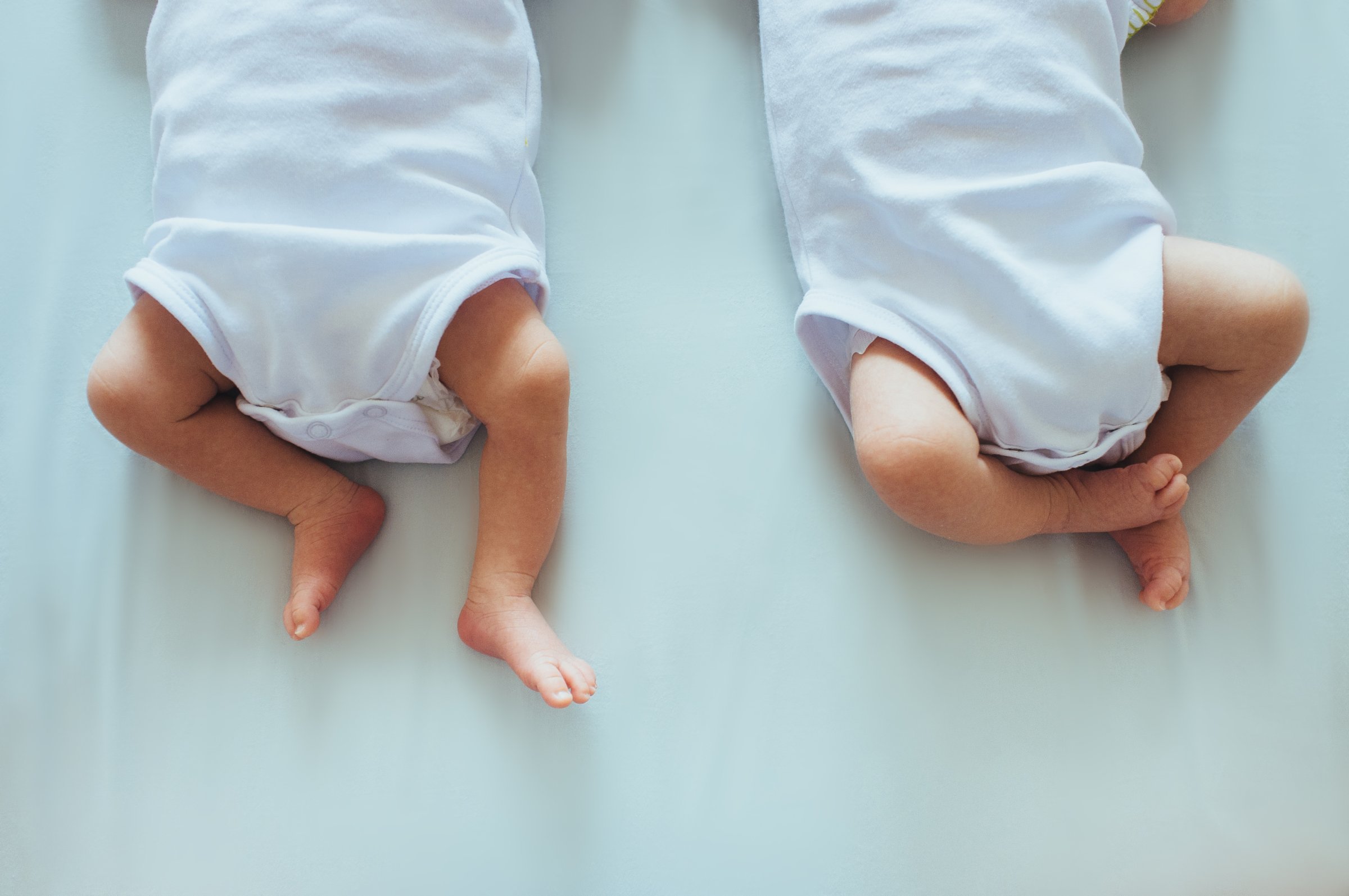 Photo of 2 babies on bed focusing on their legs.