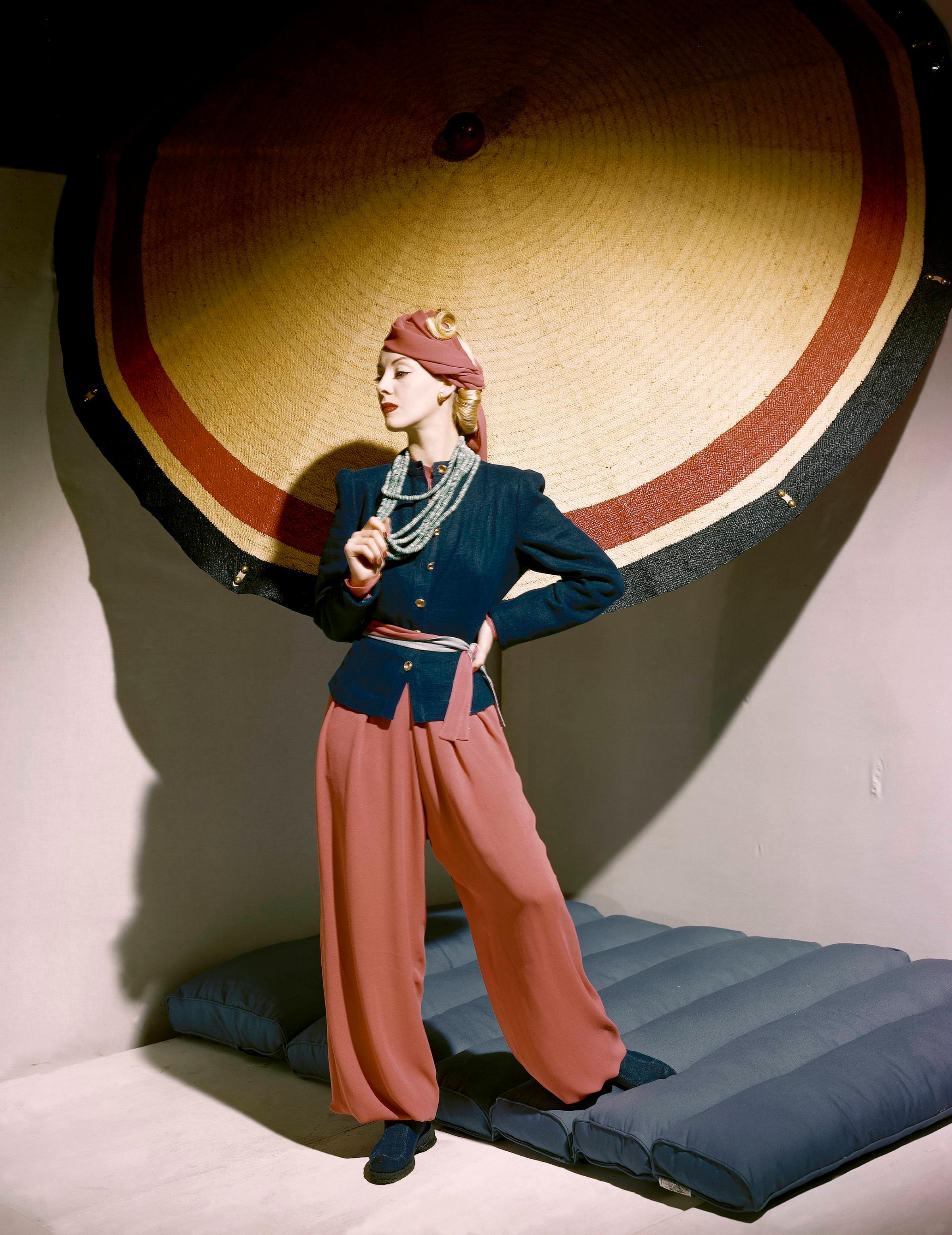 Model standing next to umbrella, wearing blue linen jacket and silk crepe pyjamas with double-layered trousers, 1939.