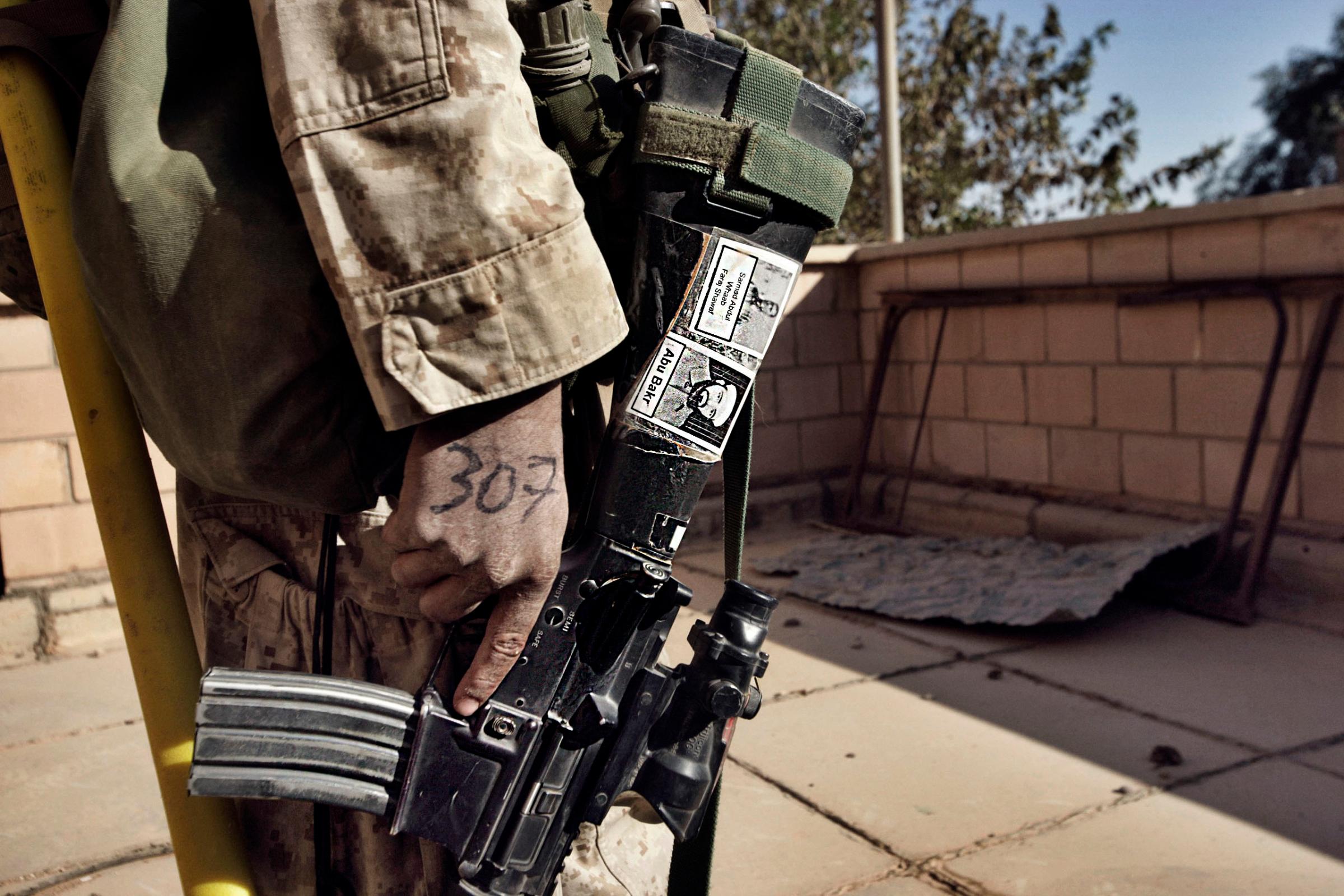 A Marine from Fox Co. 2nd Battalion 1st Marines holds his M-16 rifle with pictures of suspected insurgents during the first day of Operation Steel Curtain, an effort to stop foreign fighters from crossing into Iraq. Nov. 5, 2005.