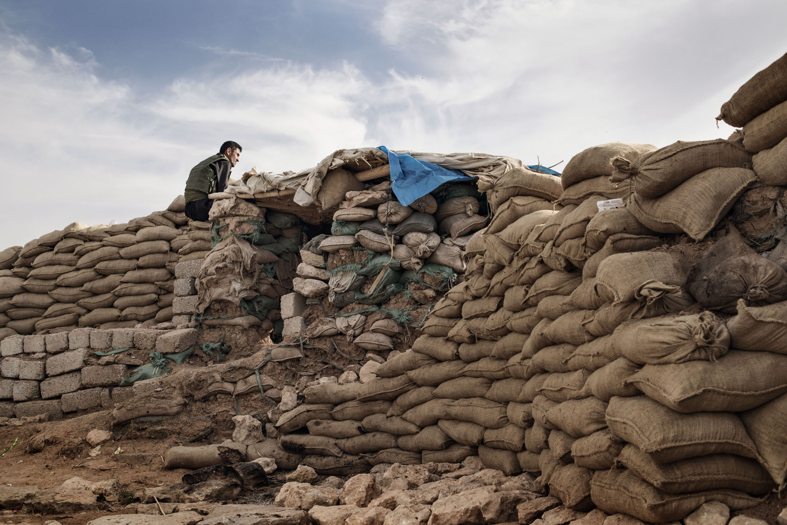 A member of the Kurdish Peshmerga armed forces sits atop sandbags, overlooking the ISIS-held city of Mosul, northern Iraq, May 9, 2016. The Kurdish fighters holding the line against ISIS are so close to ISIS positions that they can even pick up the jihadists' radio broadcasts, including propaganda and religious programing. Days earlier, the Kurdish fighters at the Bashiqa front repelled an attack that left at least two dead among their ranks.