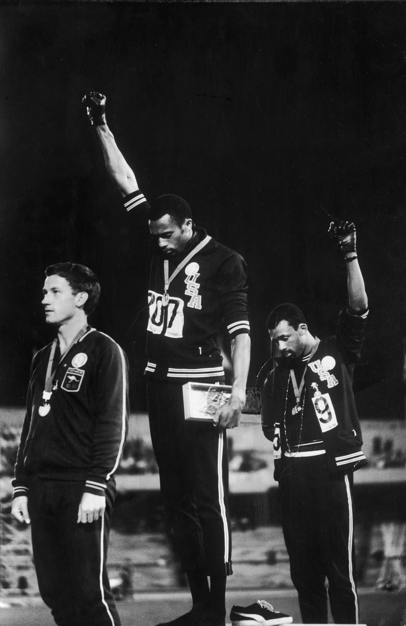 American track stars Tommie Smith (C) and John Carlos (R) standing on podium after winning gold and bronze Olympic medals, respectively, raising black-gloved fists, in support of civil rights/black power, while Australian silver medalist Peter Norman stands by at the 1968 summer Olympics in Mexico City, Mexico.