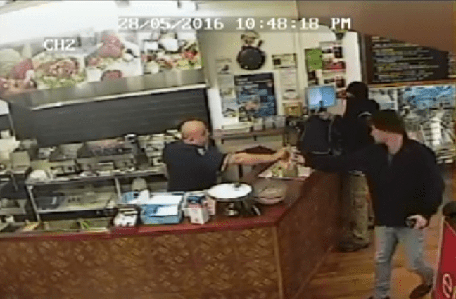 Take-out store owner serves a customer as an armed robber looks on in Christchurch, New Zealand on July 9, 2016. (Canterbury Police)