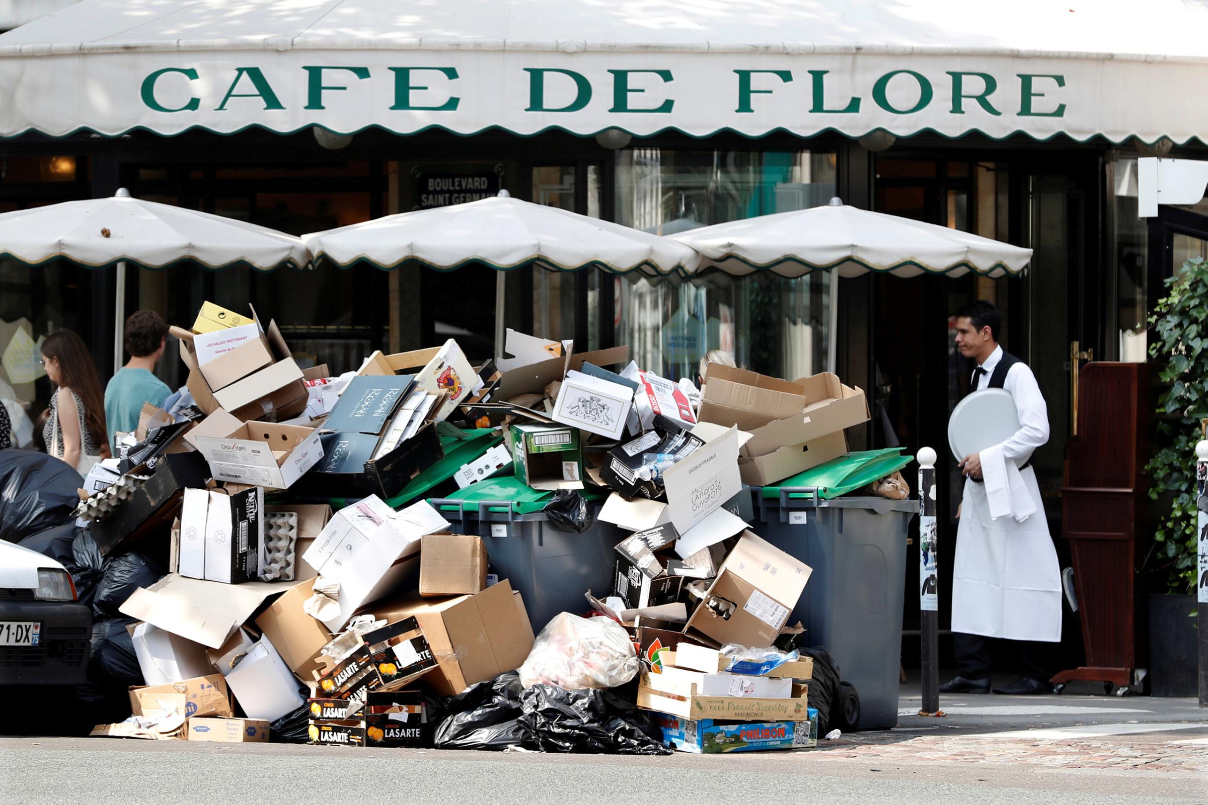 A waiter stands near a pile of rubbish bags in front of the Cafe de Flore in Paris during a strike of garbage collectors and sewer workers of the city of Paris to protest the labour reforms law proposal