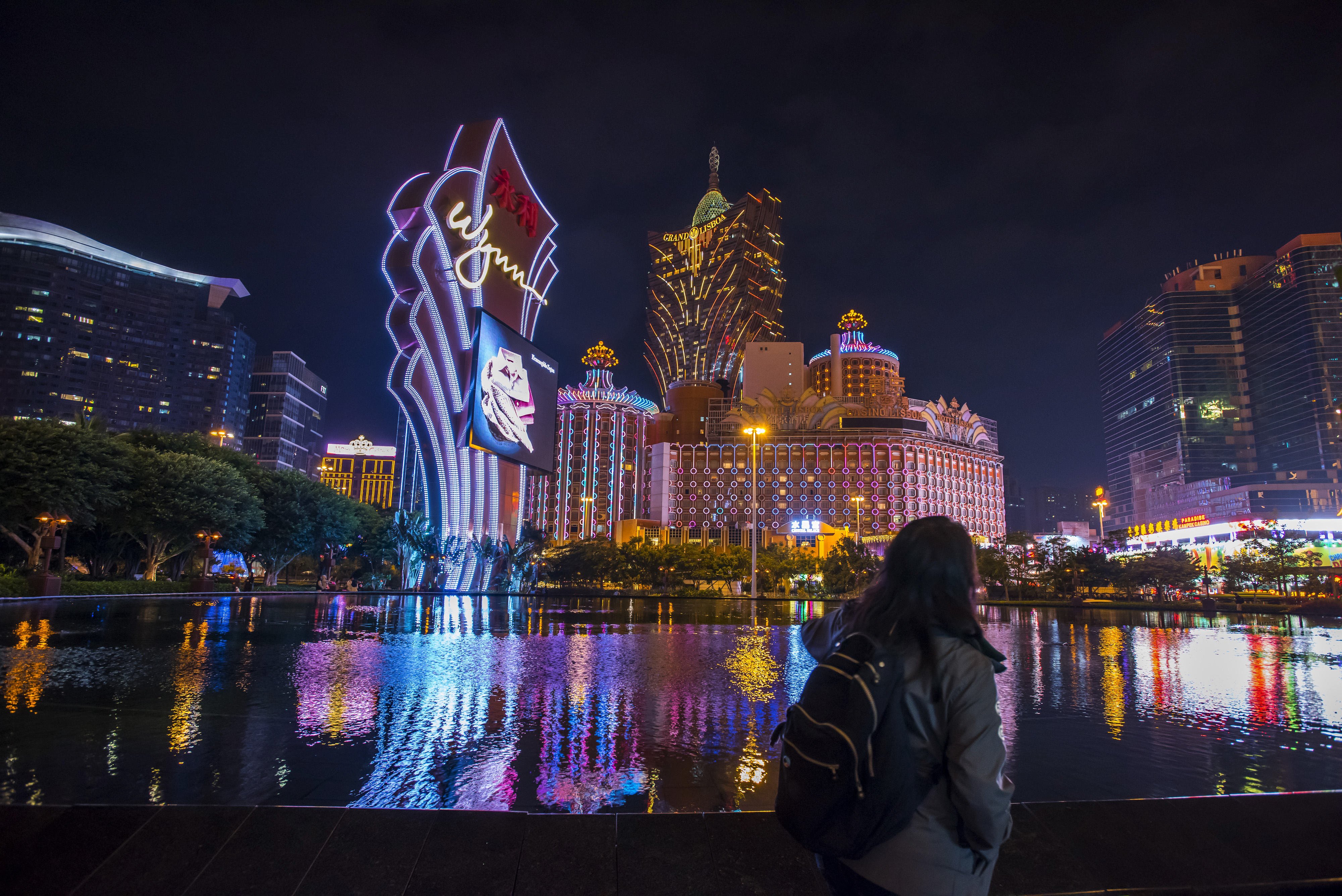 A pedestrian walks past signage for the Wynn Macau casino resort, operated by Wynn Resorts, front, as the Casino Grand Lisboa, center, stands illuminated at night in Macau on Dec. 6, 2015. Casino operators in the Chinese gambling hub of Macau saw a 32% slump in revenue in November from a year earlier and it's fallen for 18 straight months, data from the city show (Bloomberg/Getty Images)