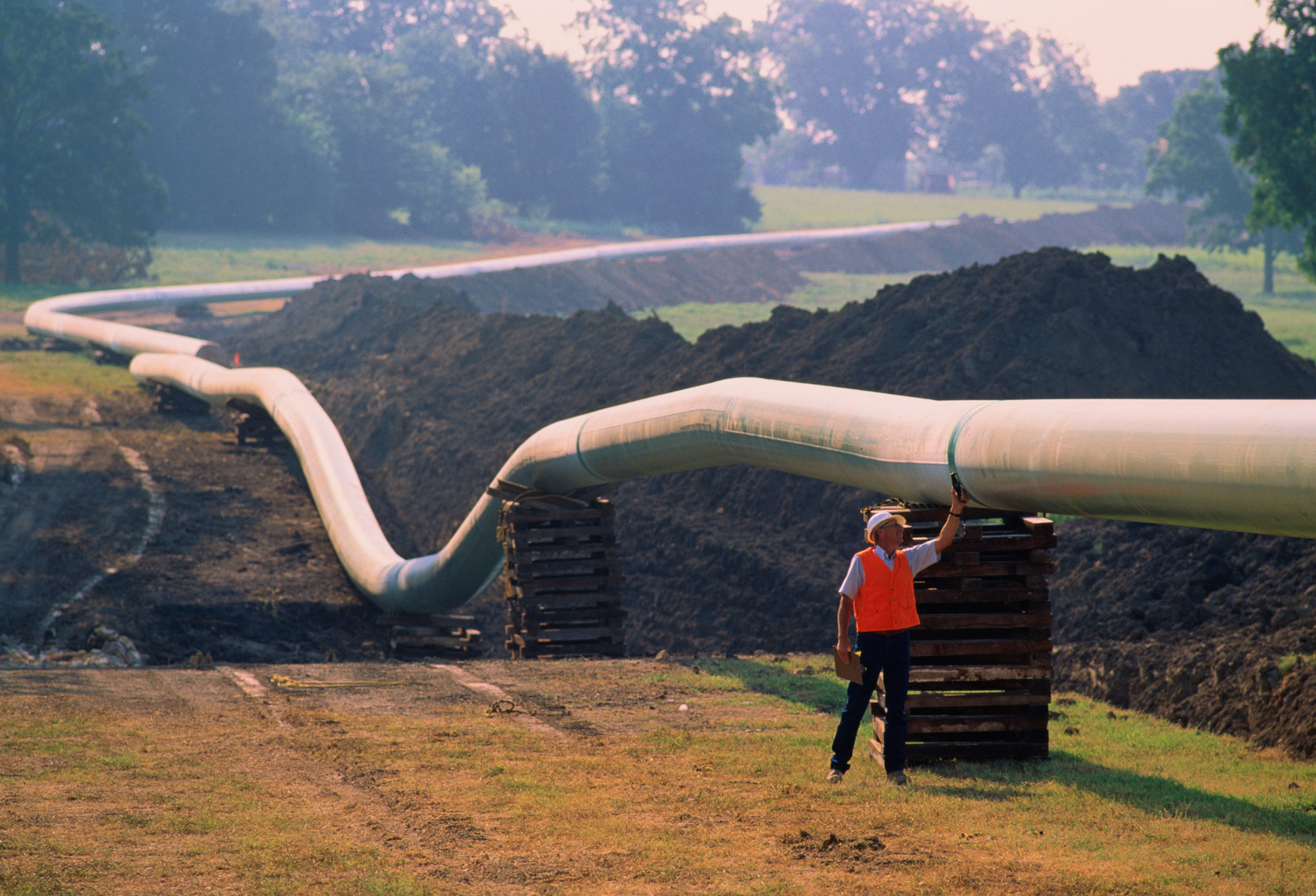 Worker checking welds on natural gas pipeline running through field (Keith Wood—Getty Images)