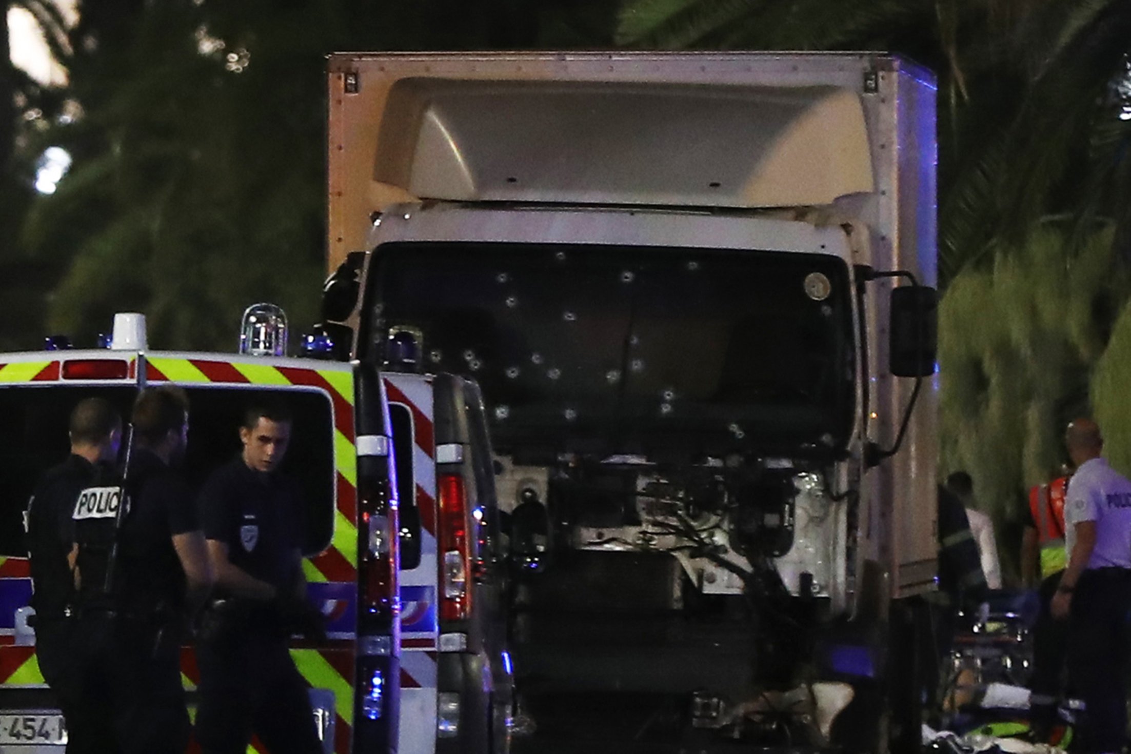Police officers stand near a van, with its windscreen riddled with bullets, that tore into a crowd leaving a fireworks display in the French Riviera town of Nice on July 14, 2016. At least 70 people were killed in the French city of Nice on Thursday after officials and authorities said a truck slammed into a crowd celebrating Bastille Day. Photographs from the immediate aftermath showed several dead bodies on a main street in the city, which lies on the coast of the Mediterranean, as well as a truck that had its windshield riddled with bullet holes. Bodies that had already been attended to were wrapped in gold sheets.