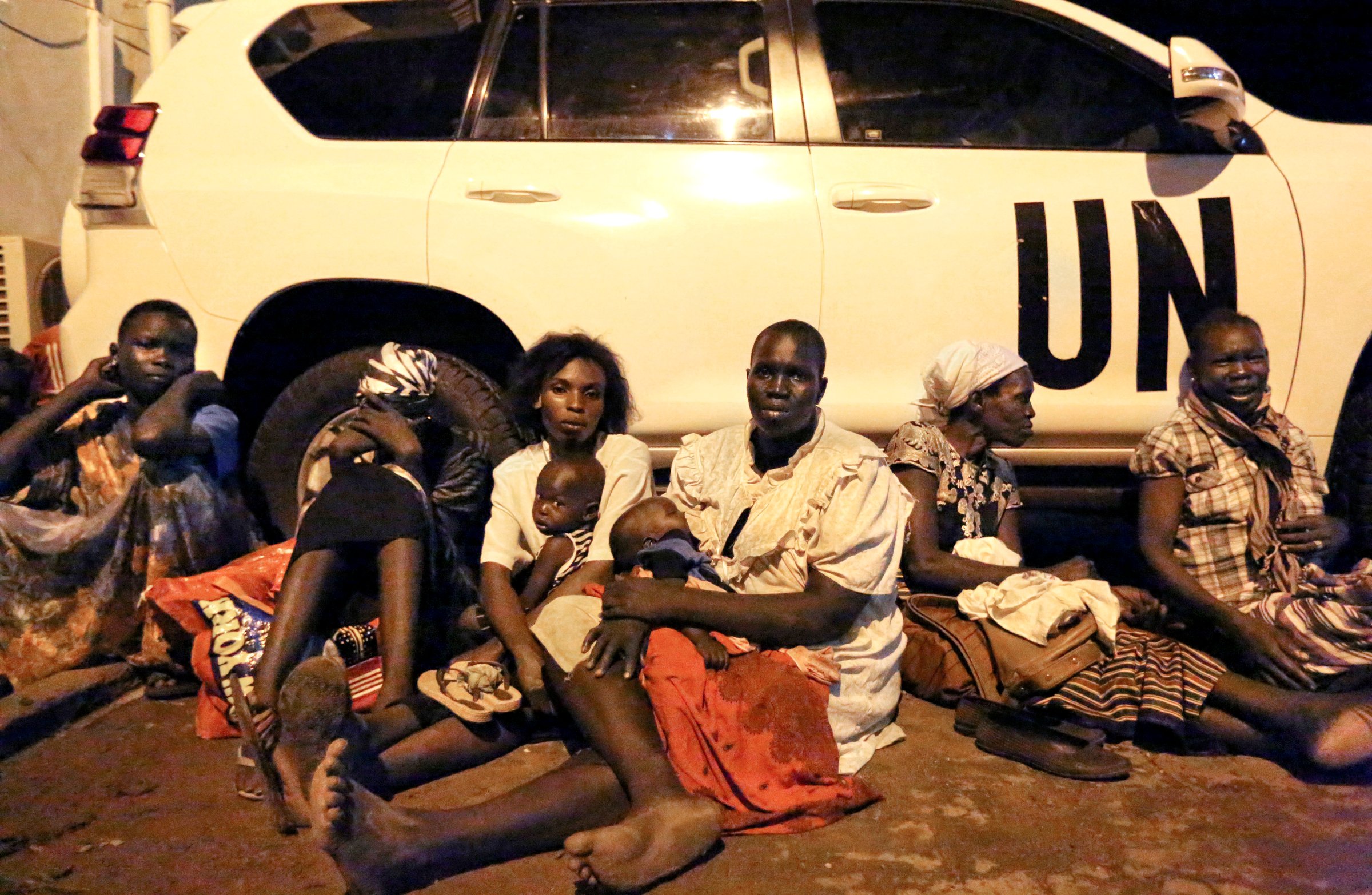 In this photo taken late Friday, July 8, 2016, and released by the United Nations Mission in South Sudan (UNMISS), women from neighboring villages rest against a U.N. vehicle as they take cover from the fighting between buildings on the perimeter of a U.N. compound in the capital, Juba.