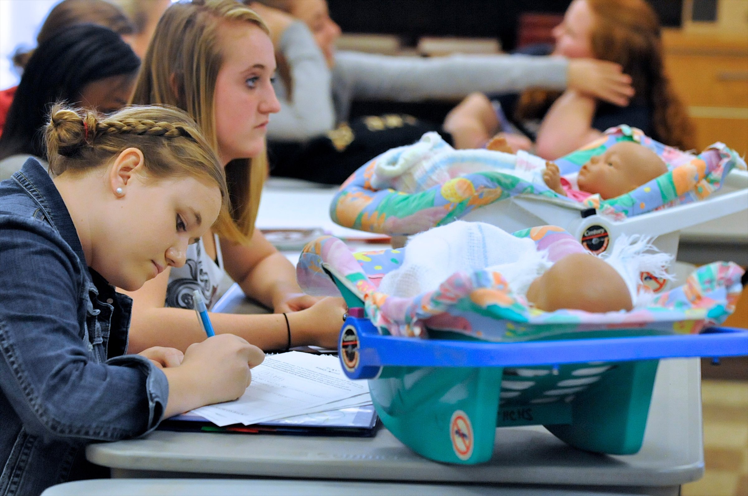 Students Sallie Norman, left, and Katie Osborne, in Catherine Gray's Child Development class, at Henderson County High, work in class with two infant simulators, in Henderson, Ky., Thursday, Oct. 6, 2011. The simulators, that students take home on weekends, are essentially baby dolls in baby carriers that cry, burp, need to be fed and need diaper changes according to a pre-set program that the students cannot control or predict. (AP Photo/The Gleaner, Mike Lawrence)