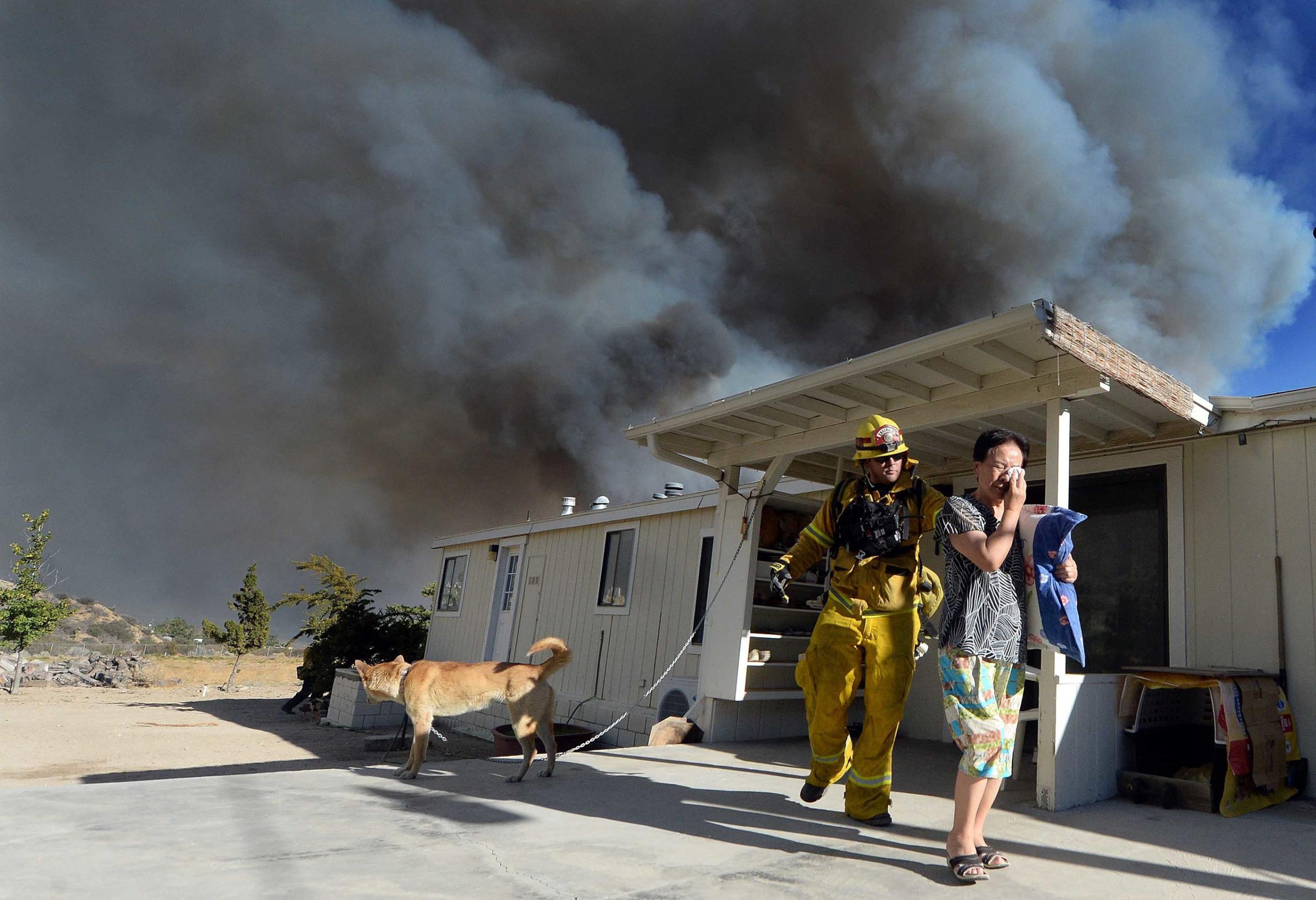 San Bernardino County Firefighter, Engineer, and Paramedic, Jeremy Pendergraft, helps a couple evacuate out of their home as she cries off of Hess Rd. as a wildfire off of Hwy 138 quickly approaches in San Bernardino, Calif., Aug. 16, 2016.