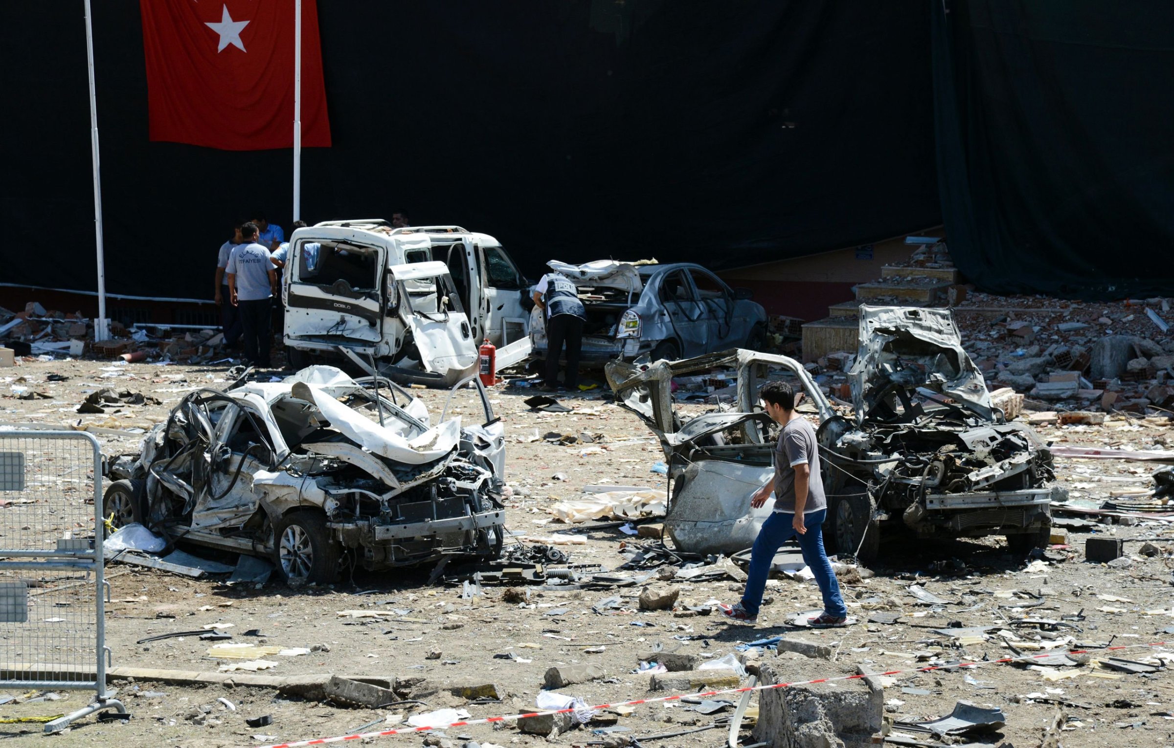 Turkish rescue workers stand by the wreckage of a vehicle as a Turkish police officer inspects a destroyed car and a man walks among the remains at the blast scene following a car bomb attack on a police station in the eastern Turkish city of Elazig, on Aug. 18, 2016.