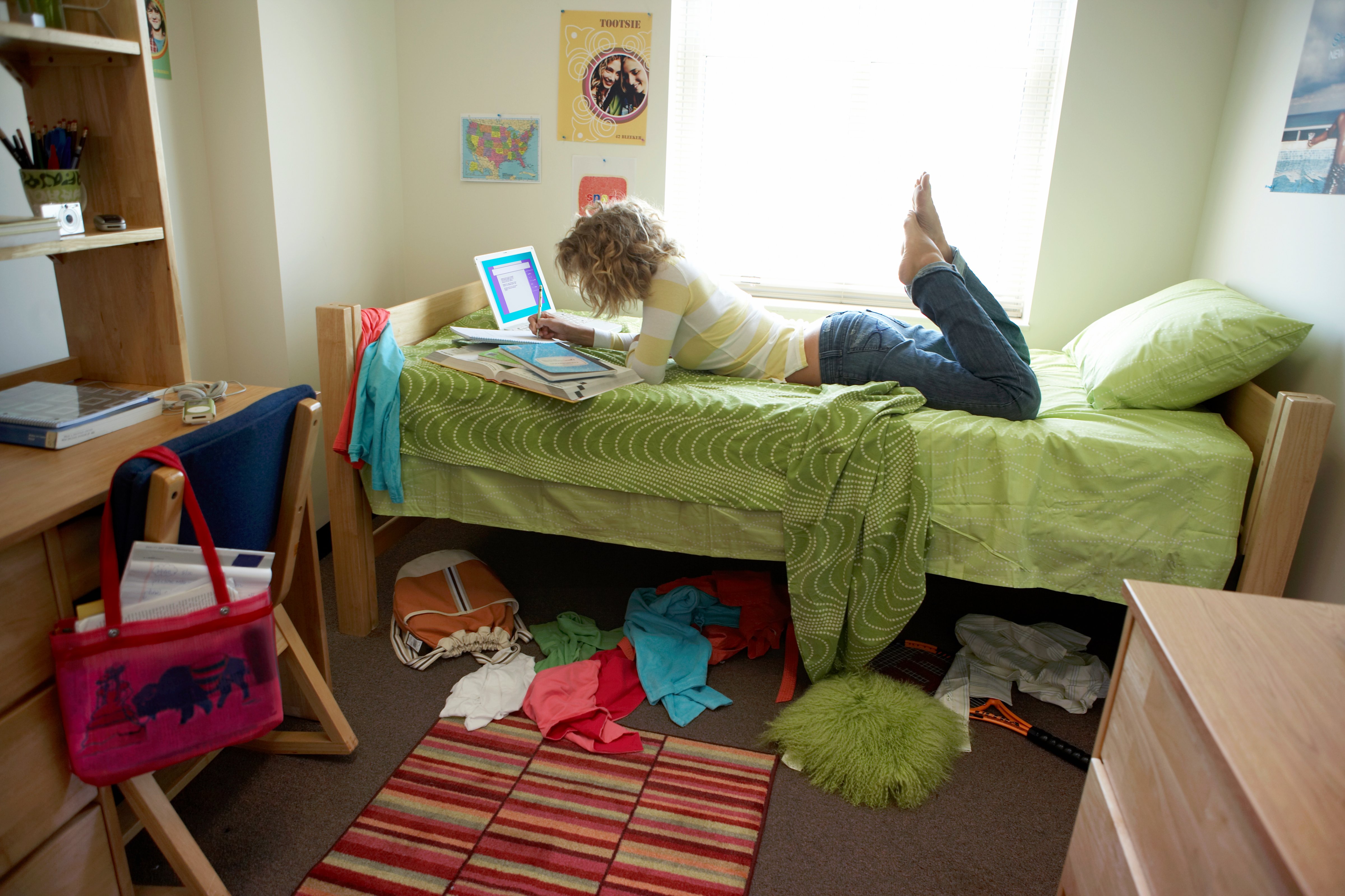 Young woman lying on bed in student dorm, writing in exercise book