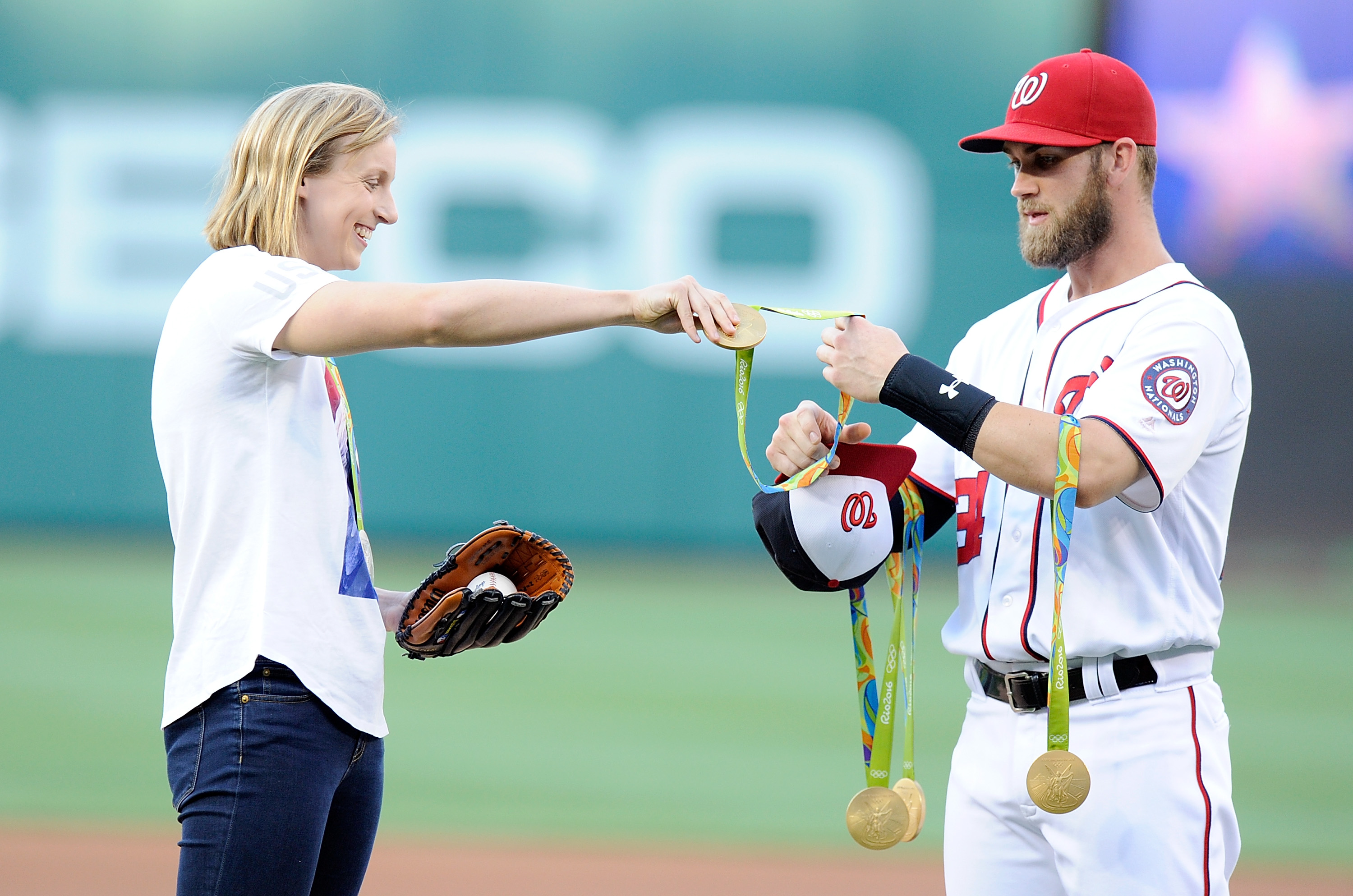Katie Ledecky hands her Olympic medals to Bryce Harper before throwing out the opening pitch at Nationals Park on Aug. 24, 2016 in Washington, DC. (Greg Fiume—Getty Images)