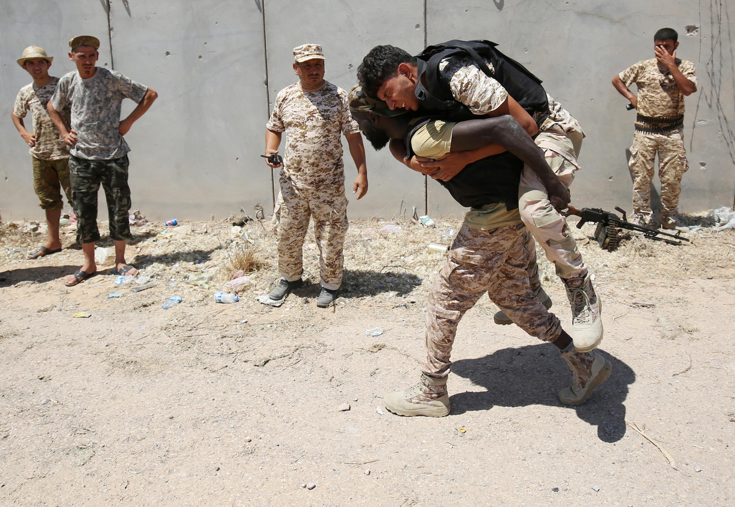 A fighter of the Libyan forces allied with the U.N.-backed unity government carries a wounded man during a battle against ISIS fighters in Sirt, Libya, on July 31, 2016.