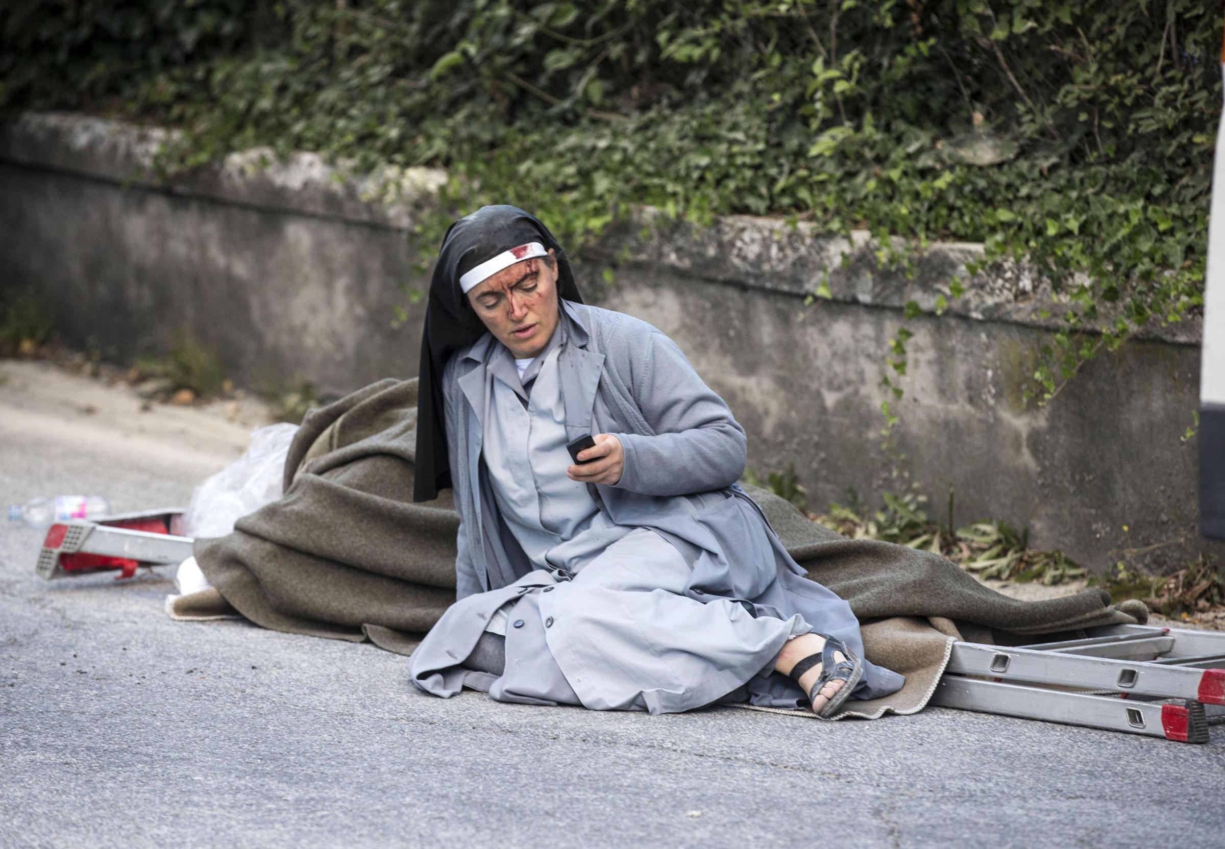A nun checks her mobile phone as she lies near a victim laid on a ladder following an earthquake in Amatrice Italy, Aug. 24, 2016.