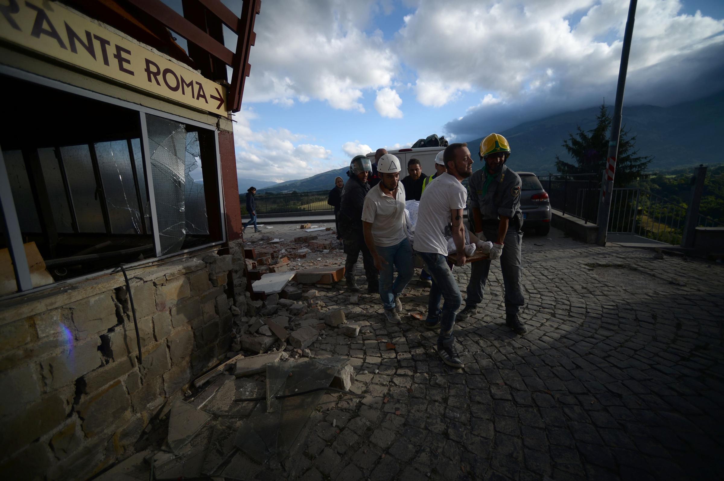 Rescuers carry a man on a stretcher in front of a damaged building after a strong earthquake hit central Italy, in Amatrice on Aug. 24, 2016.