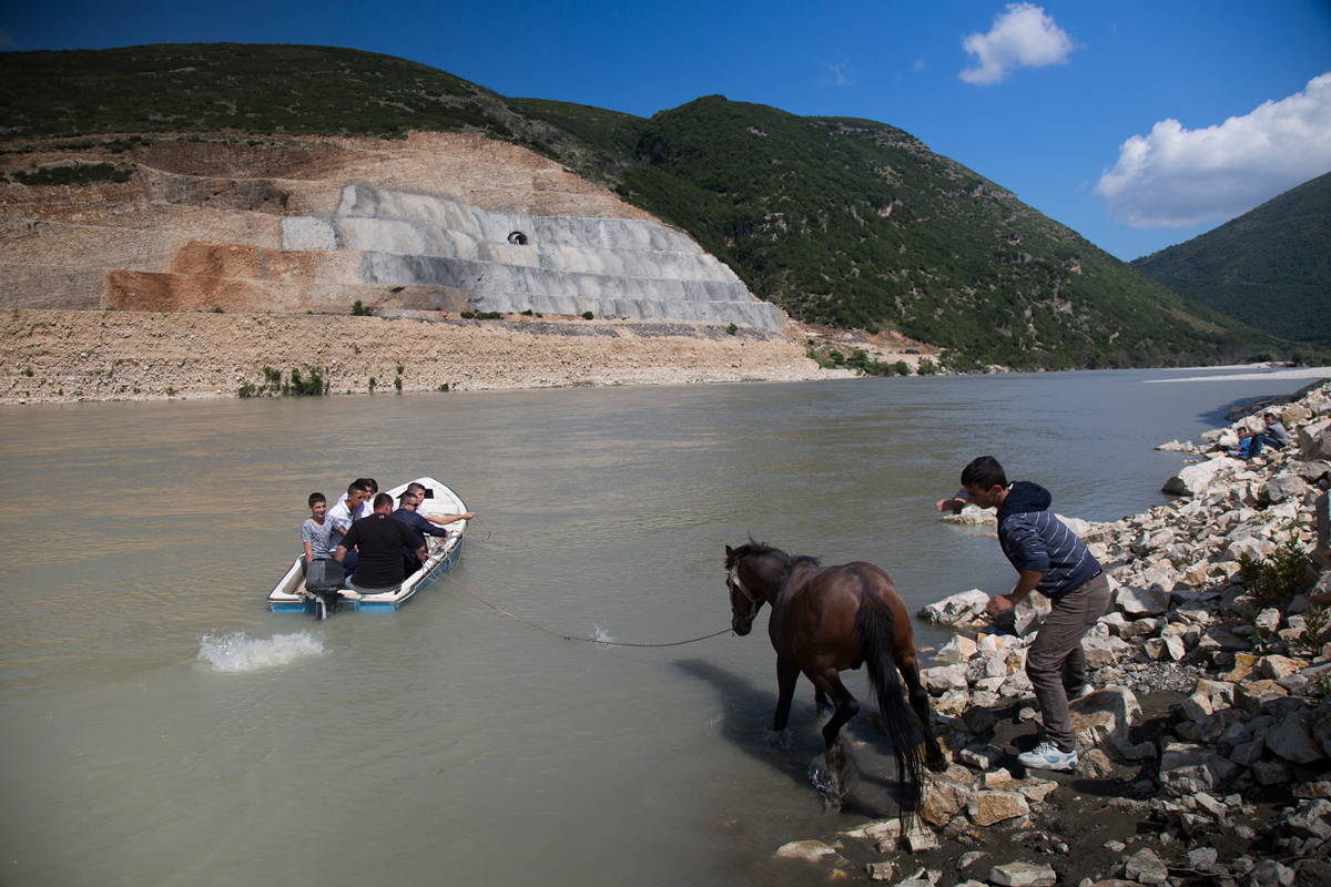 A boy slaps a horse to get it into the fast-moving waters of the Vjosa River to swim it to the other side in May 2016. The walls of the stalled Kalivac dam rise in the background, cut into the living rock of the surrounding hills. (John Wendle)