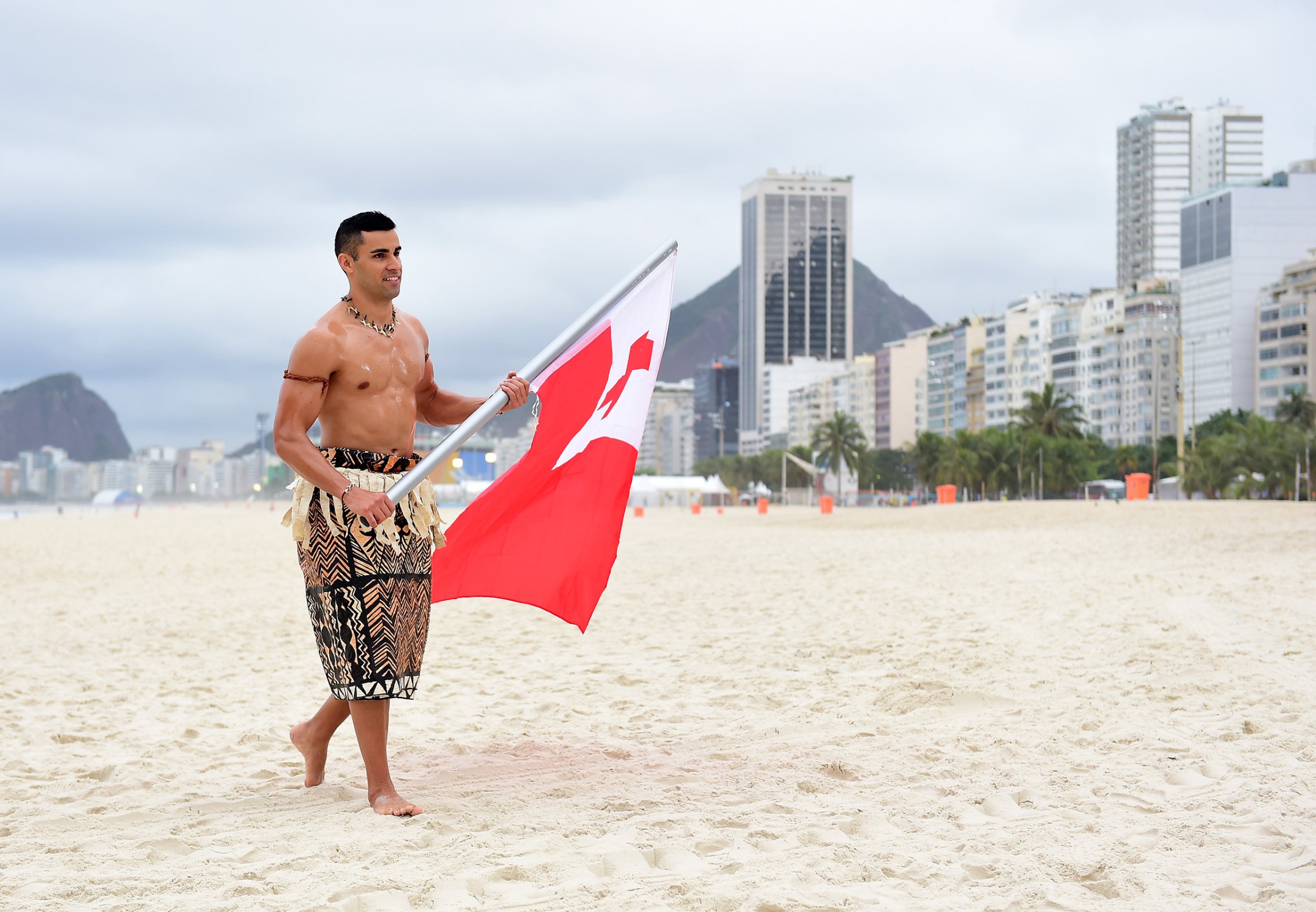 RIO DE JANEIRO, BRAZIL - AUGUST 08: Pita Taufatofua of Tonga walks along the sand with his country's flag to the NBC Today show set at Copacabana Beach on August 8, 2016 in Rio de Janeiro, Brazil. (Photo by Harry How/Getty Images)