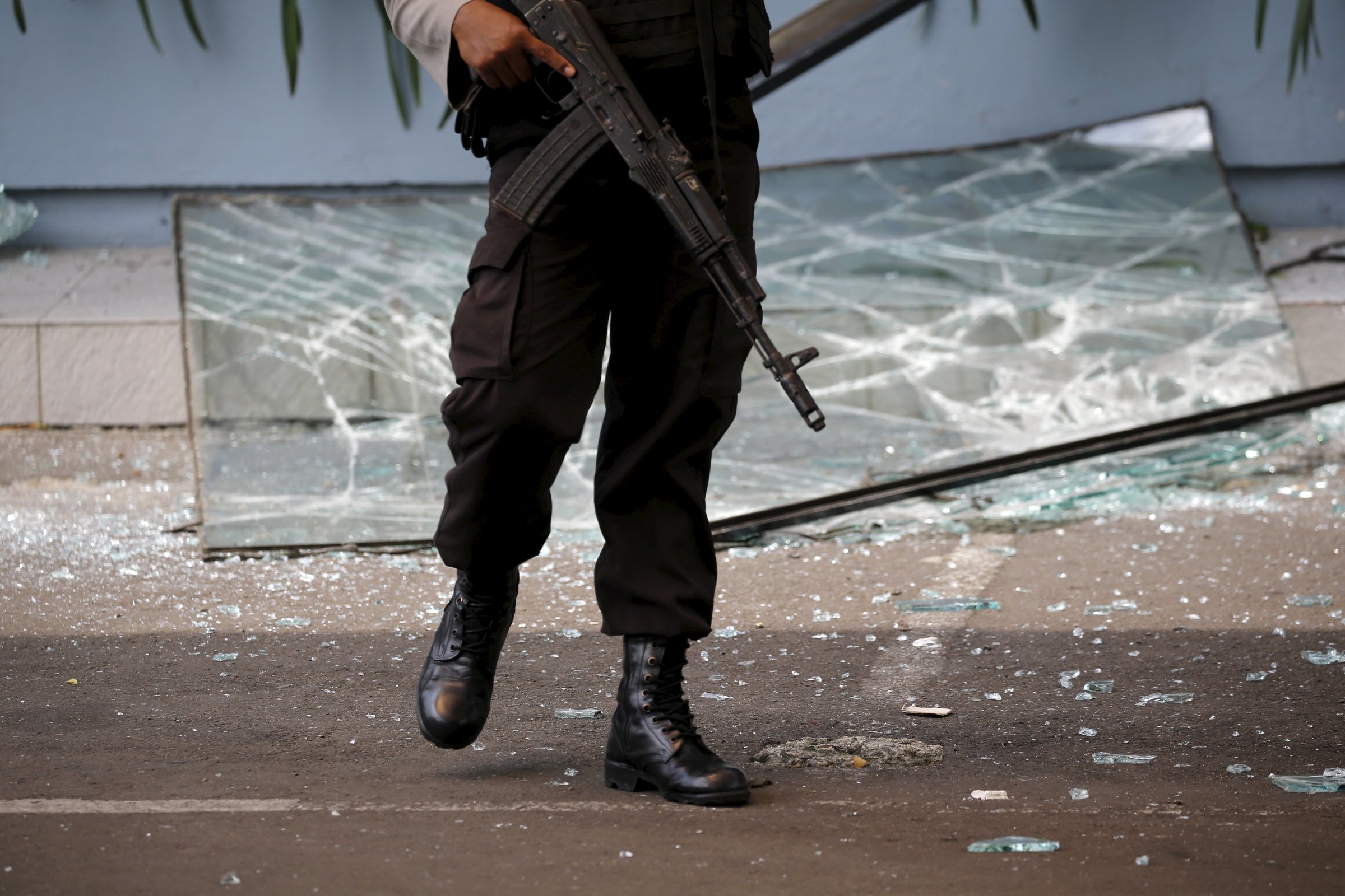 An Indonesian policeman holds a weapon while walking near a broken glass window from a Starbucks outlet in Jakarta