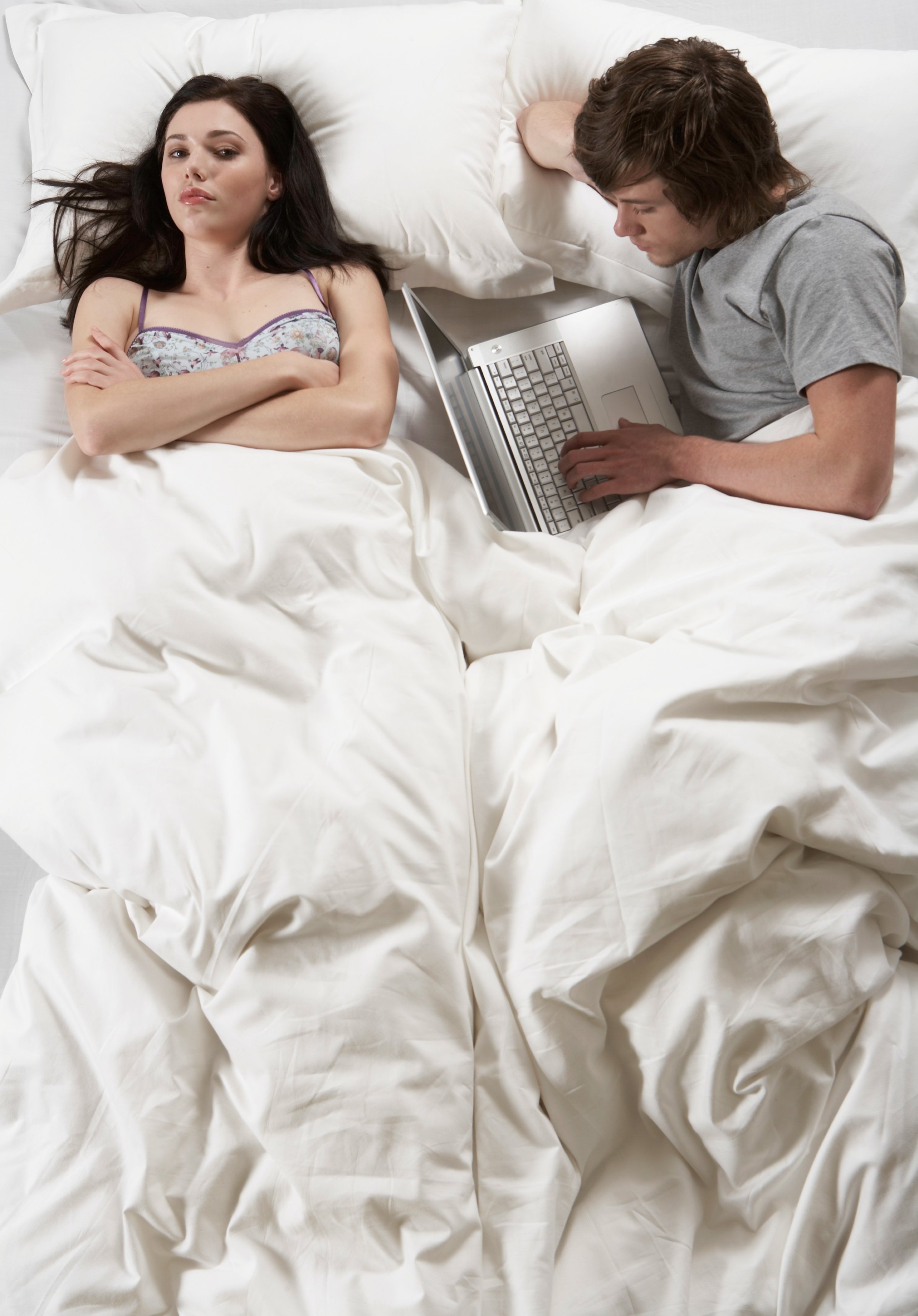 Young man and woman lying in bed, man using laptop, overhead view