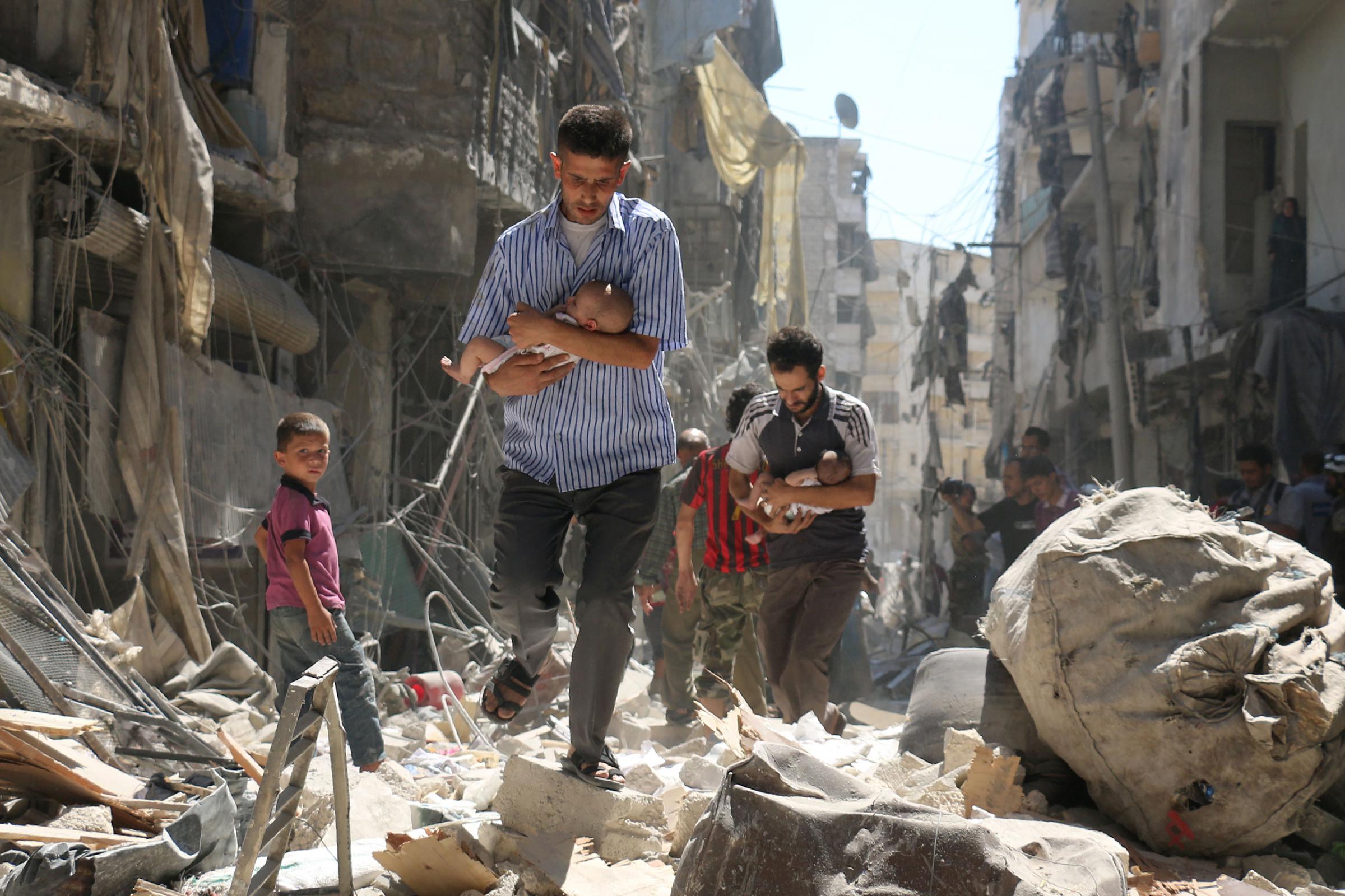 Syrian men carrying babies make their way through the rubble of destroyed buildings following a reported airstrike on the rebel-held Salihin neighborhood of Aleppo on Sept. 11, 2016.